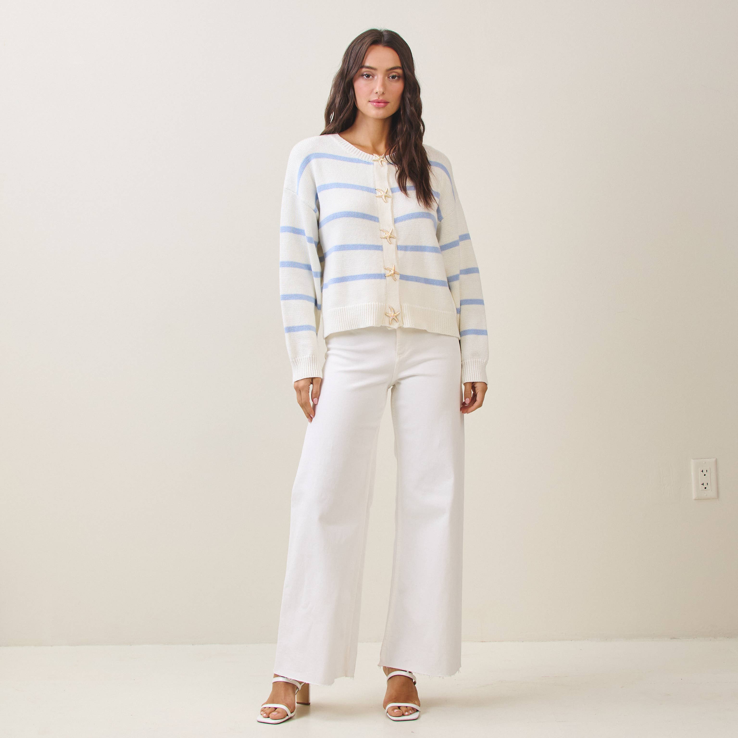 Woman wearing a striped cardigan and white pants against a plain background