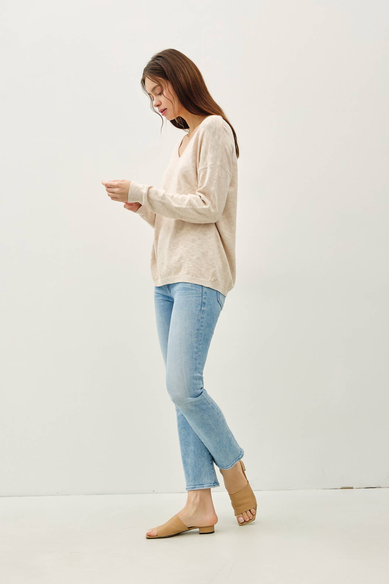 Woman wearing a beige sweater and light blue jeans against a white background
