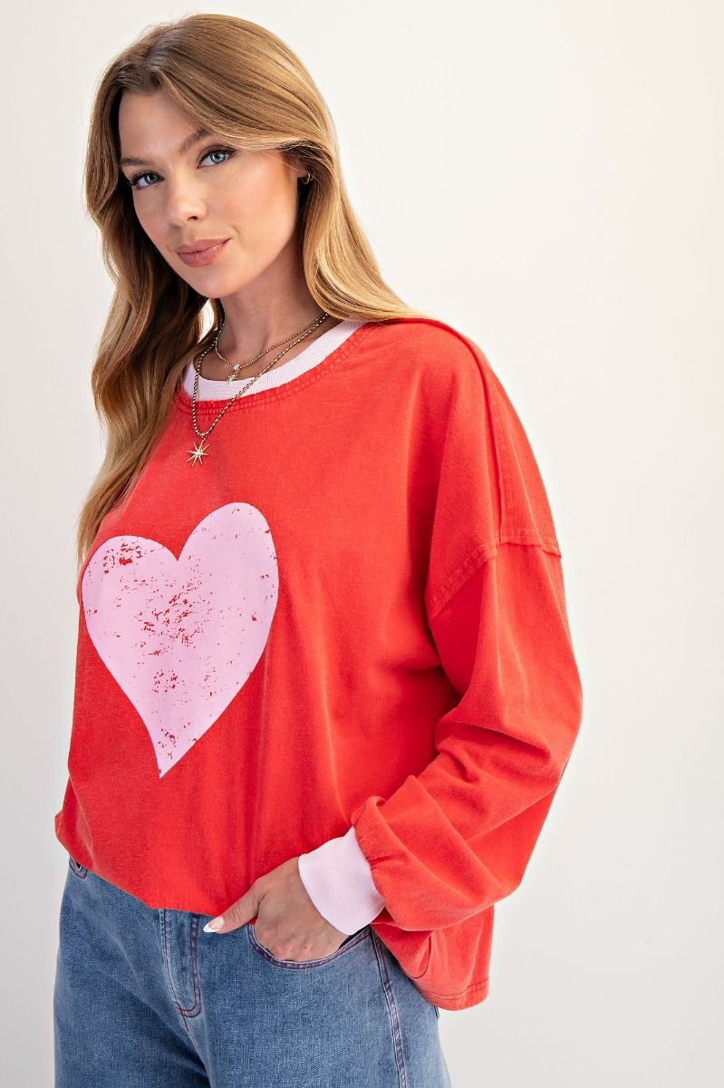 Woman wearing a red sweatshirt with a pink heart design on a plain background