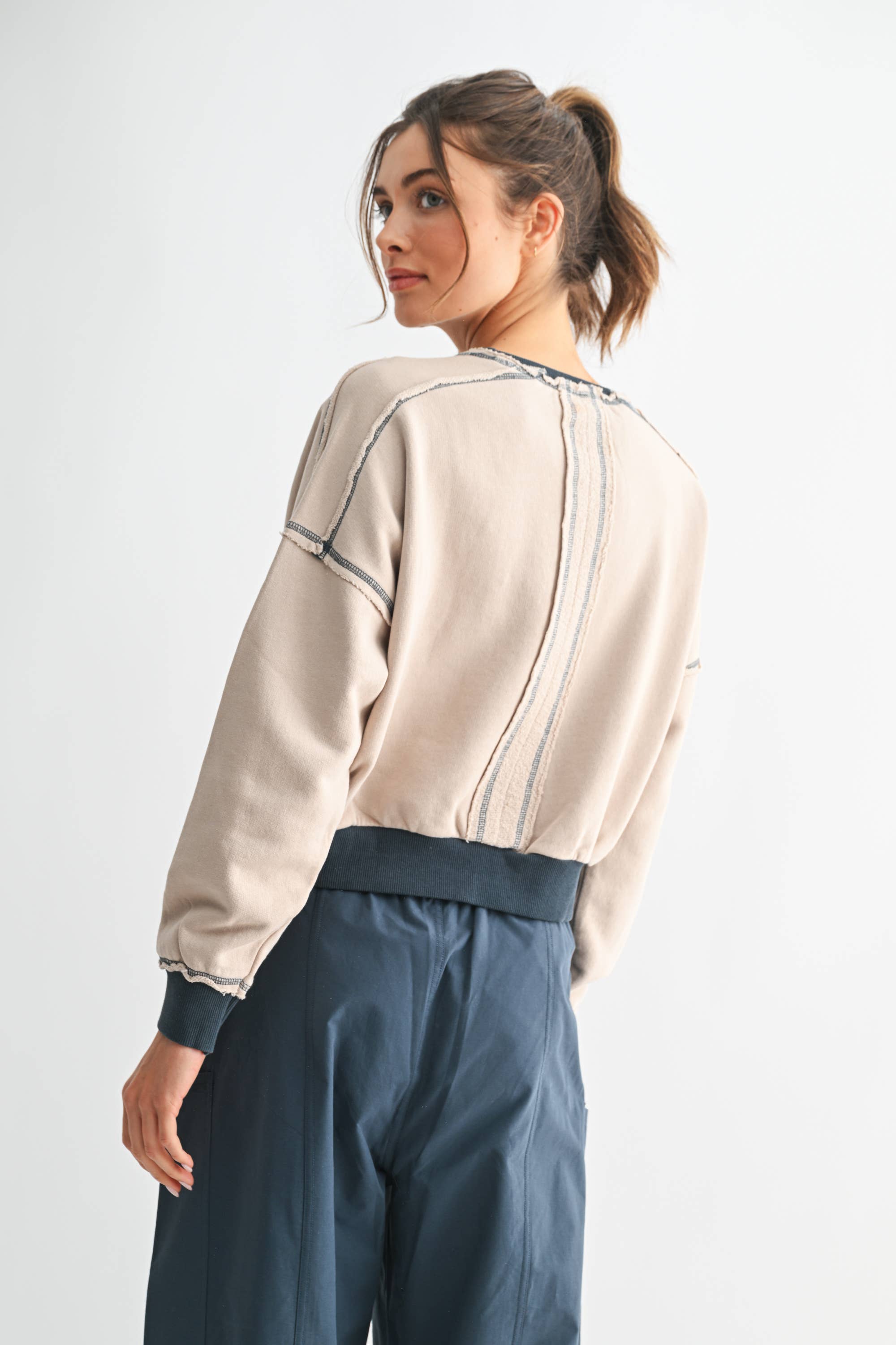 Woman wearing a beige sweatshirt and blue pants on a white background