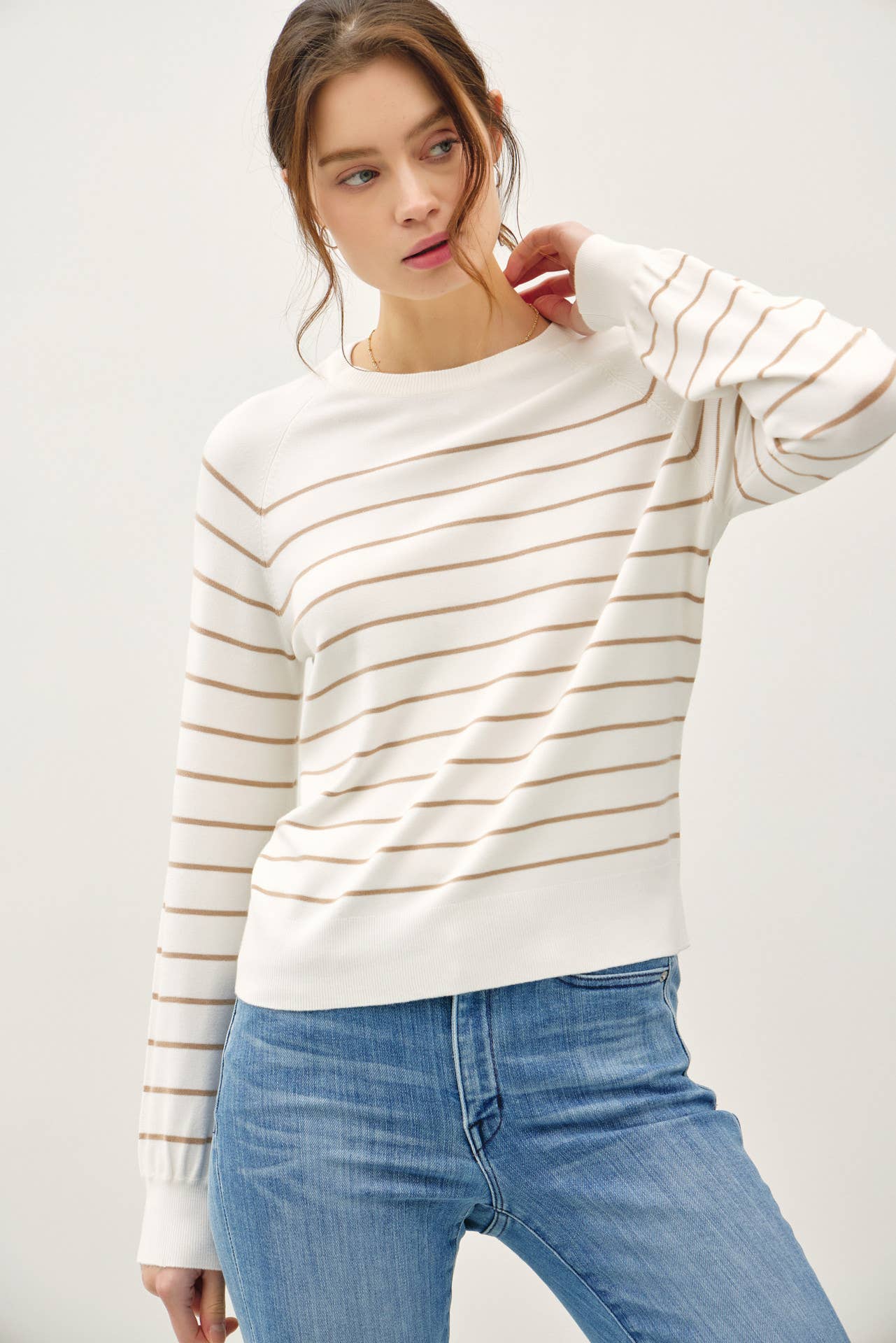 Woman wearing a white and beige striped sweater with blue jeans on a plain background