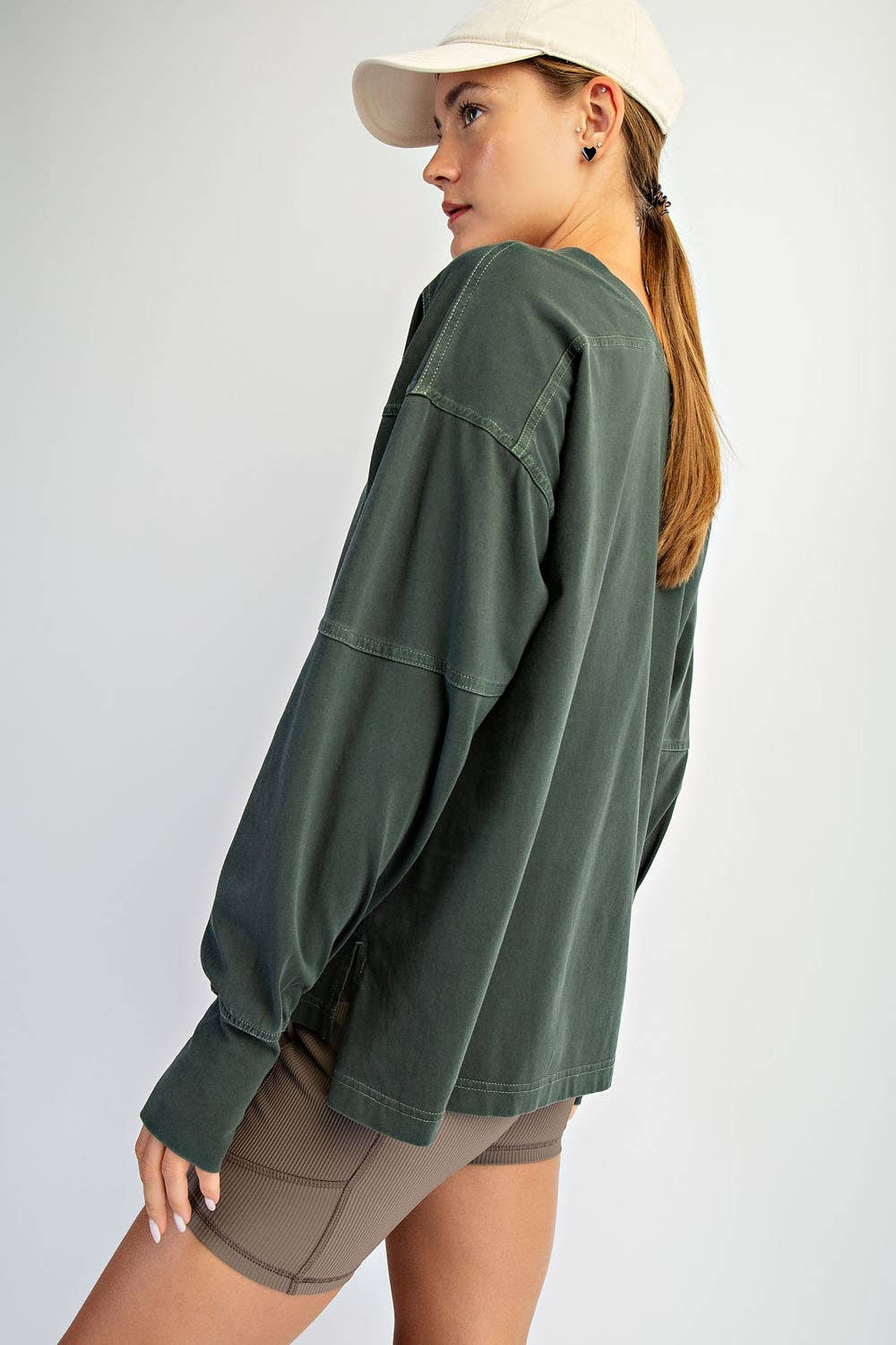 Person wearing a green long-sleeve top and beige cap on a white background