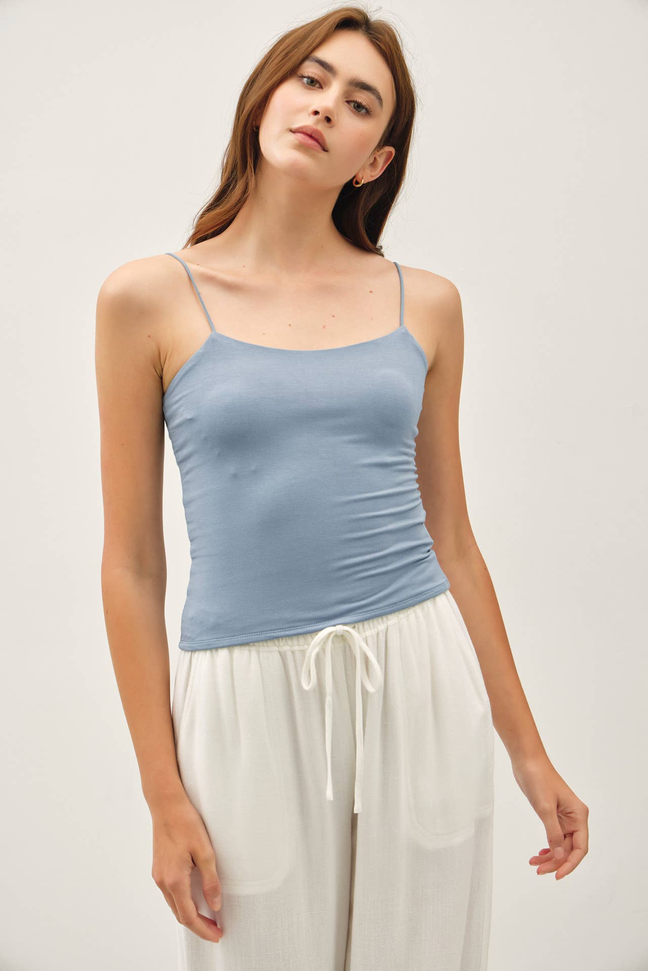Woman wearing a light blue tank top and white pants against a plain background