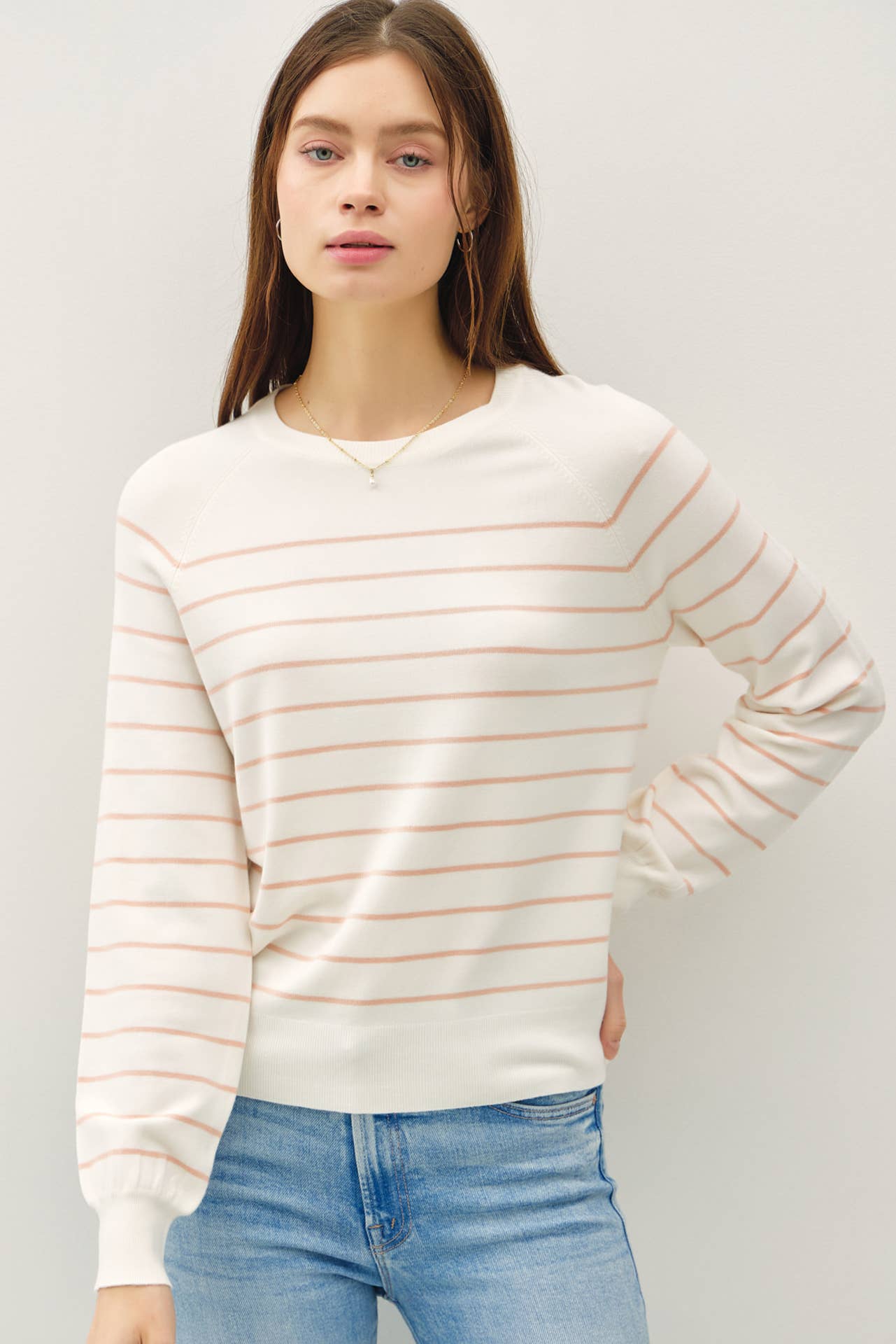 Woman wearing a white sweater with thin orange stripes against a plain background