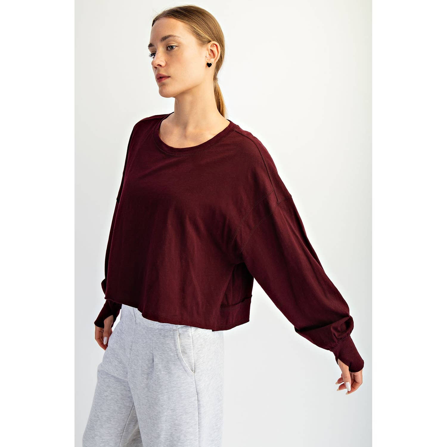 Woman wearing a burgundy sweatshirt and white pants on a light gray background