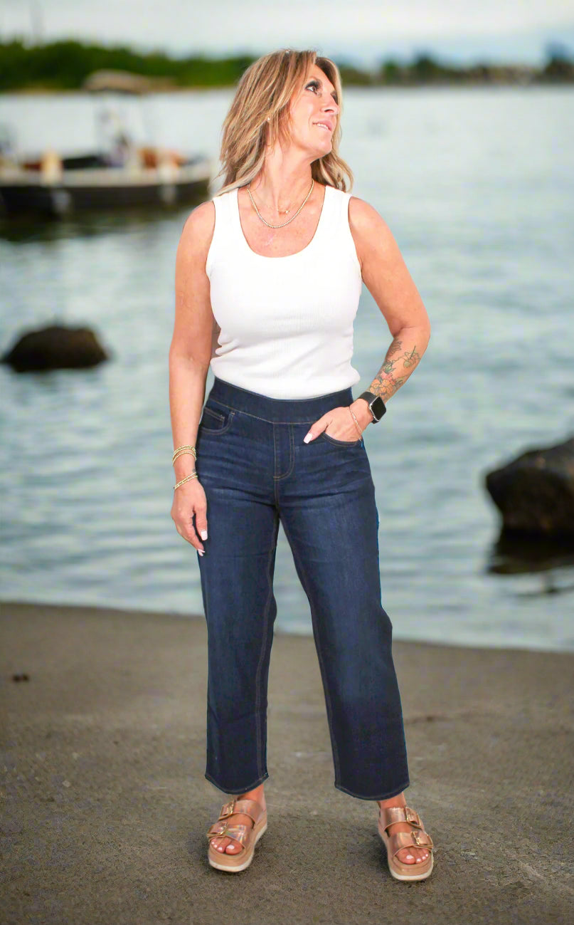 Woman wearing a white tank top and blue jeans against a white background