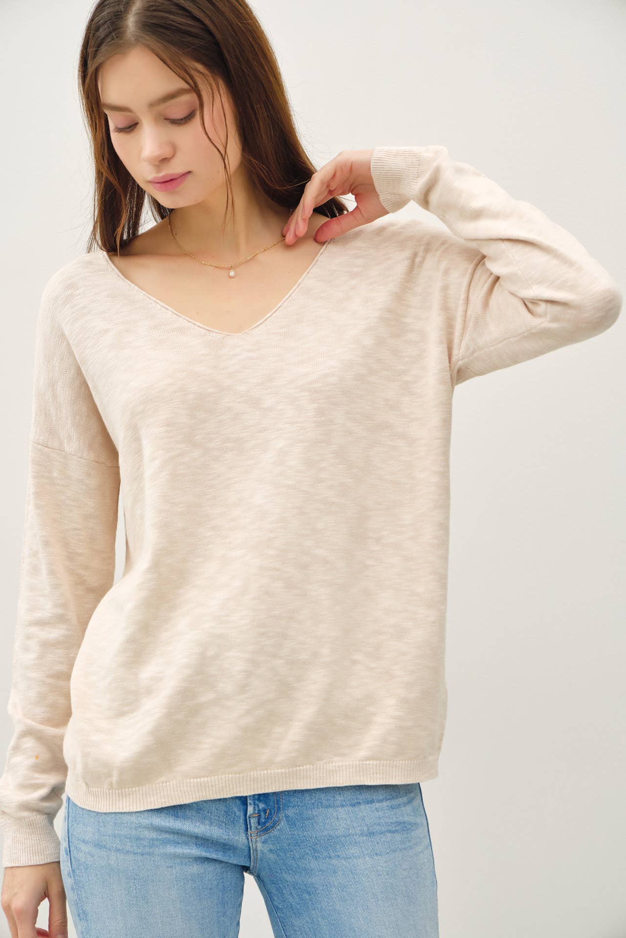 Woman wearing a beige sweater and blue jeans against a white background