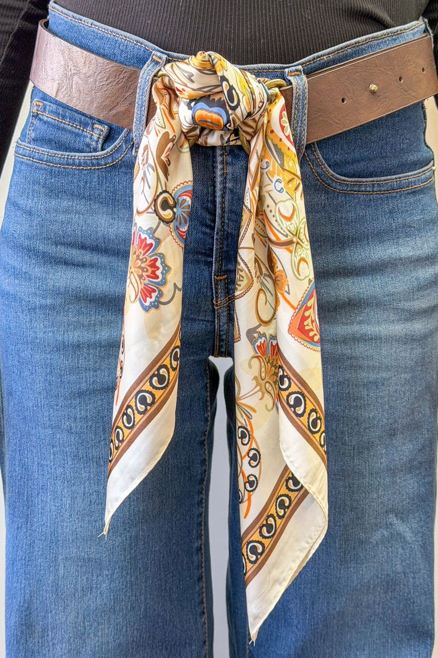 Person wearing a patterned scarf tied around their waist with jeans and a brown belt.