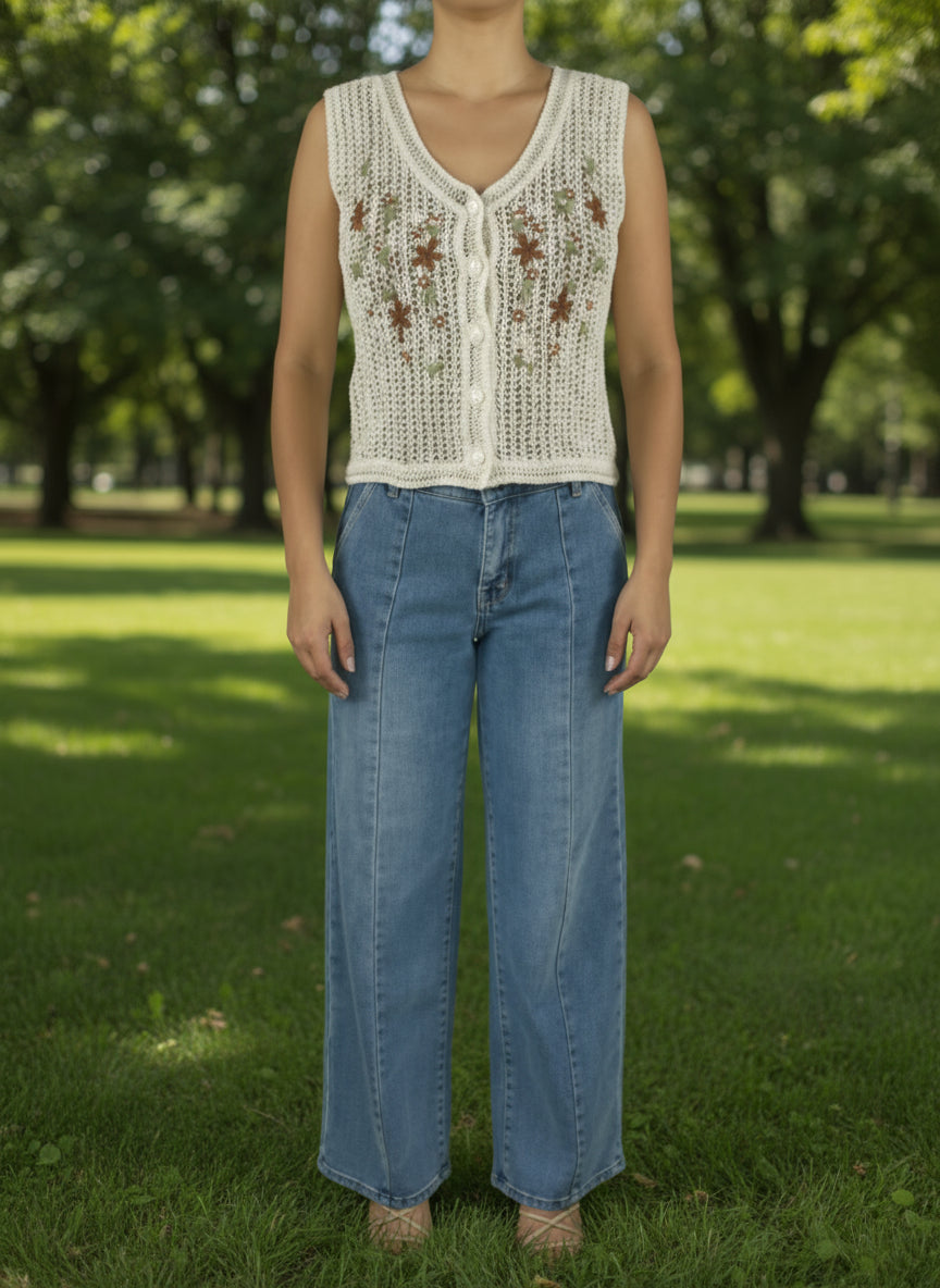 Person wearing a sleeveless crochet top with floral patterns and blue jeans on a white background