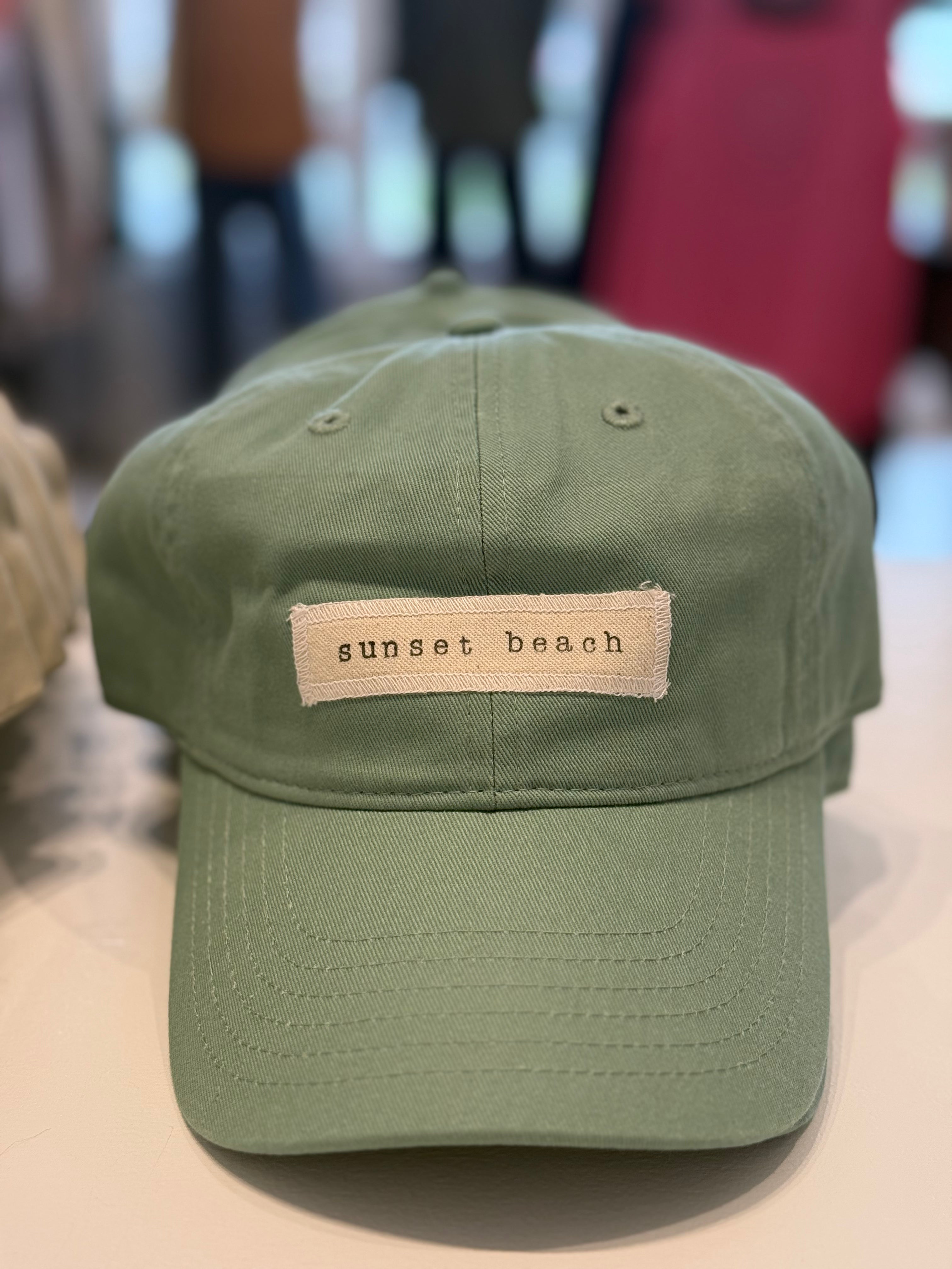 Green cap with 'sunset beach' patch on a blurred background