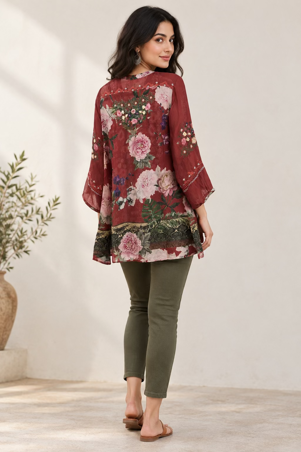 A long-sleeve tunic blouse with a red base and a large pink and green floral print, hanging on a black hanger against a white wall.