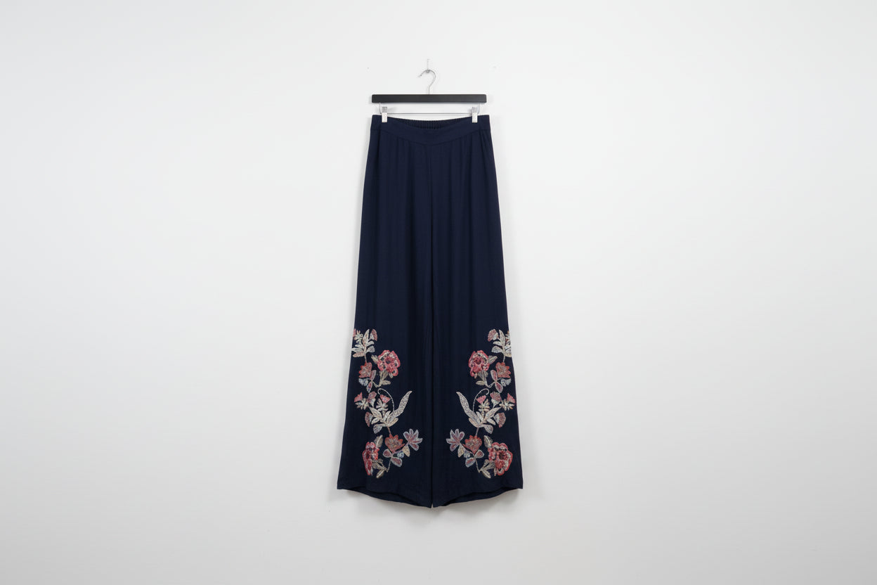 Navy blue skirt with floral embroidery hanging on a white wall.