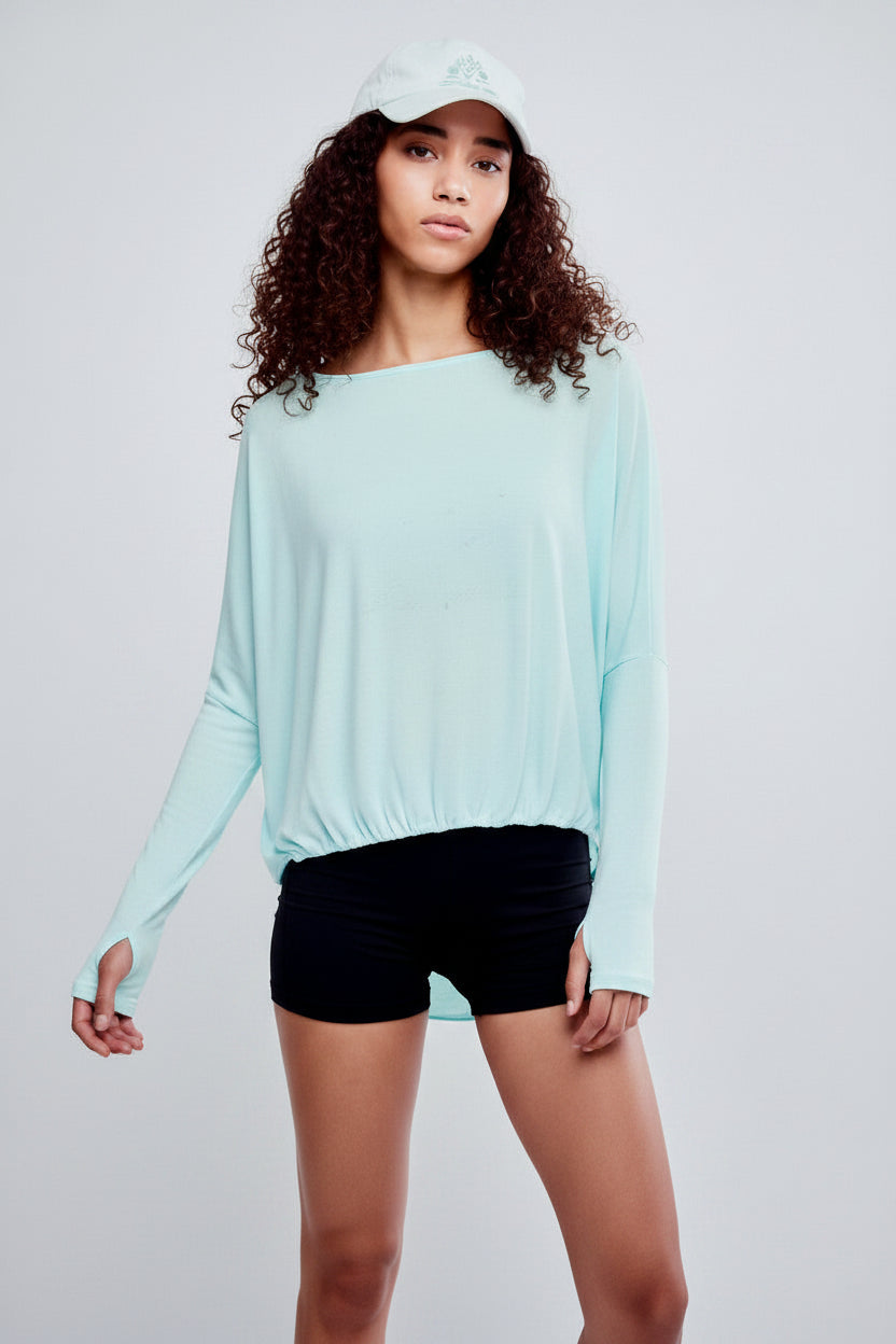 Person wearing a light blue long-sleeve top and black shorts against a plain background