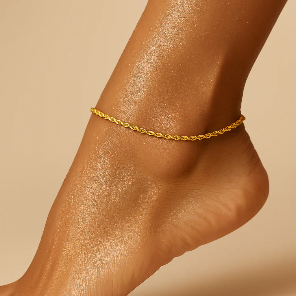 Gold anklet on a foot against a beige background