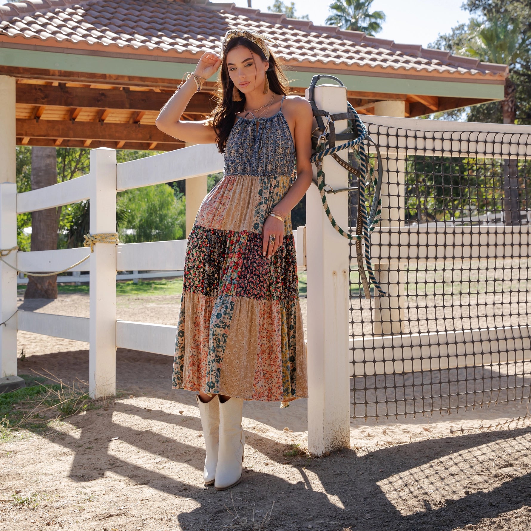 Woman in a patterned dress standing next to a wooden fence with a gazebo in the background.