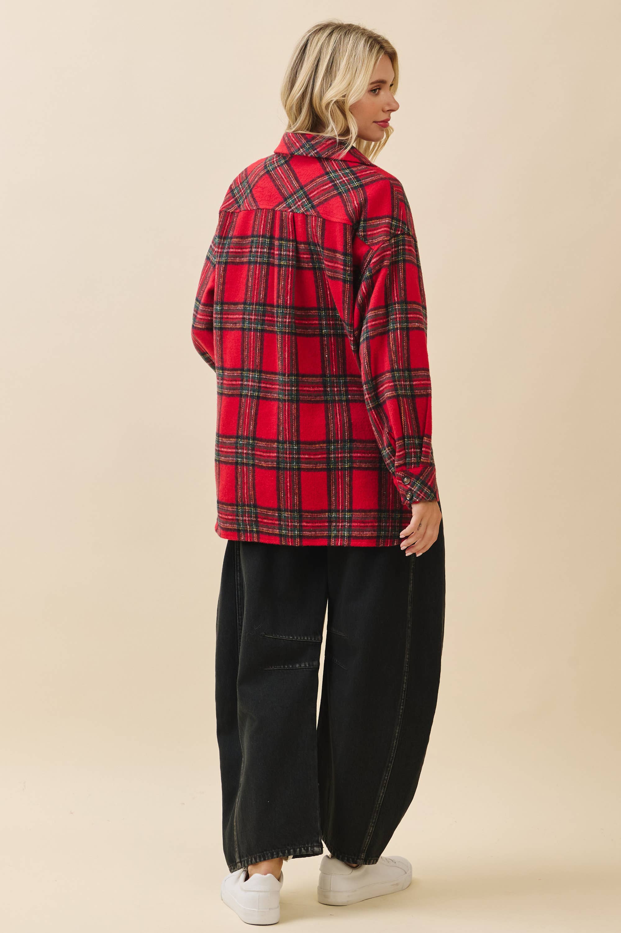 Person wearing a red plaid shirt and black pants on a beige background