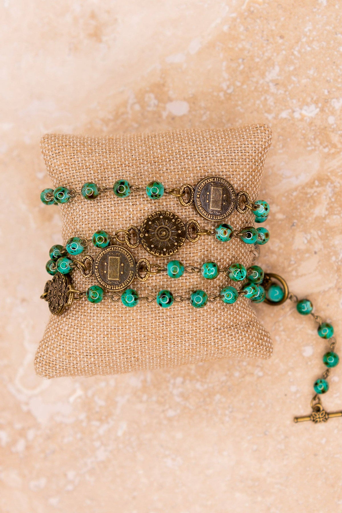 Green and gold rosary on a textured beige surface