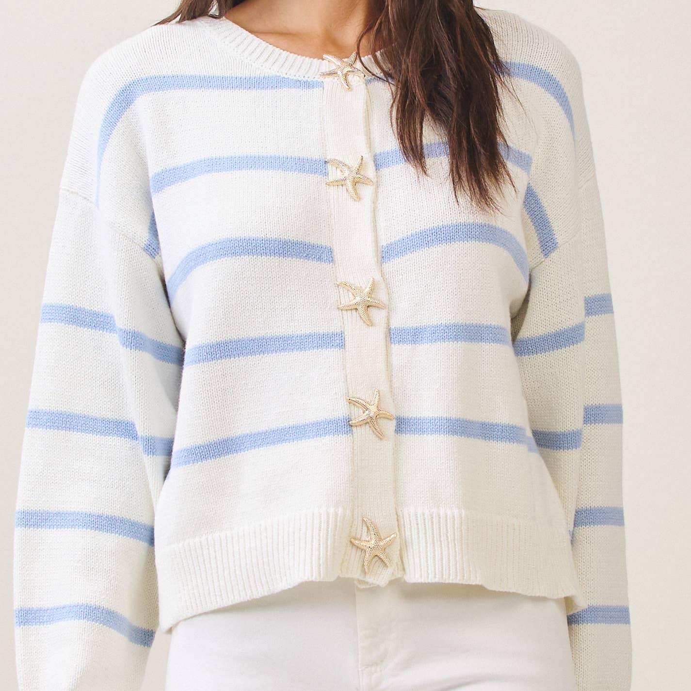 White sweater with blue stripes and starfish buttons on a plain background
