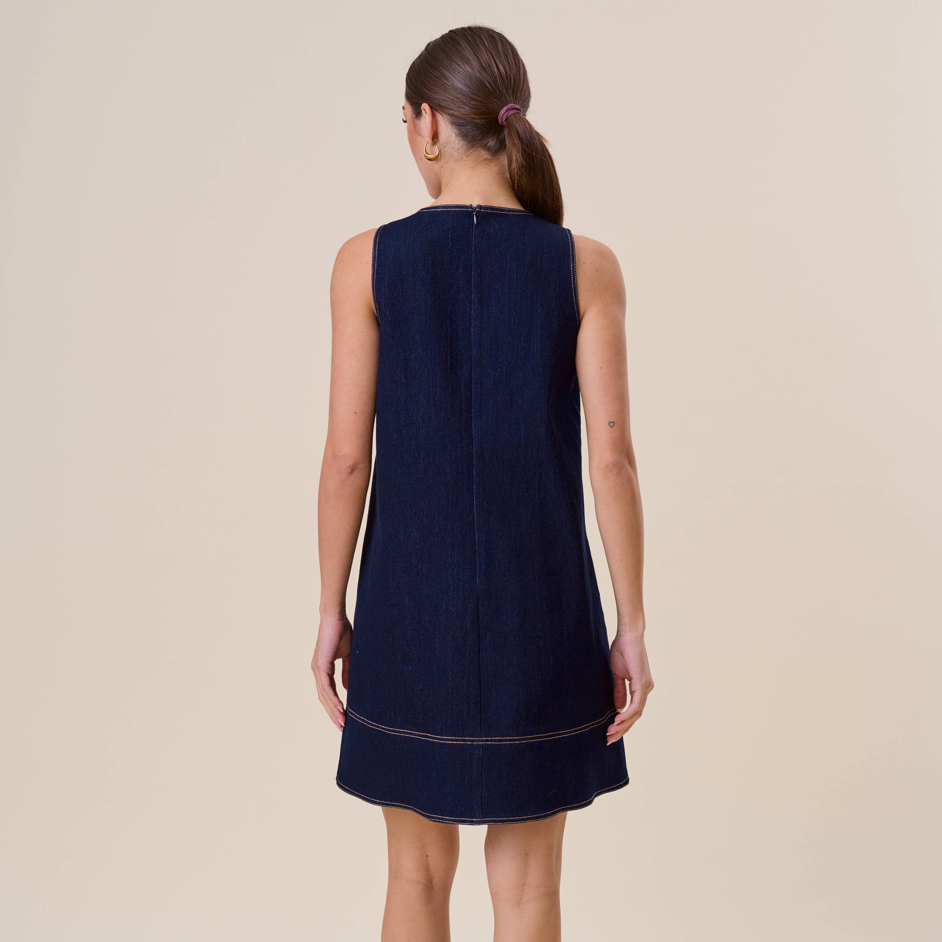 Woman wearing a navy sleeveless dress against a beige background