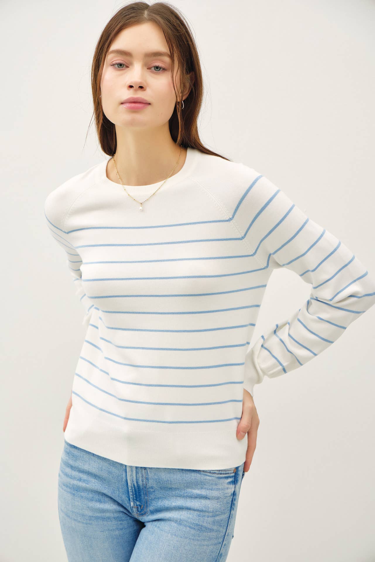 Woman wearing a white sweater with blue stripes and light blue jeans against a plain background