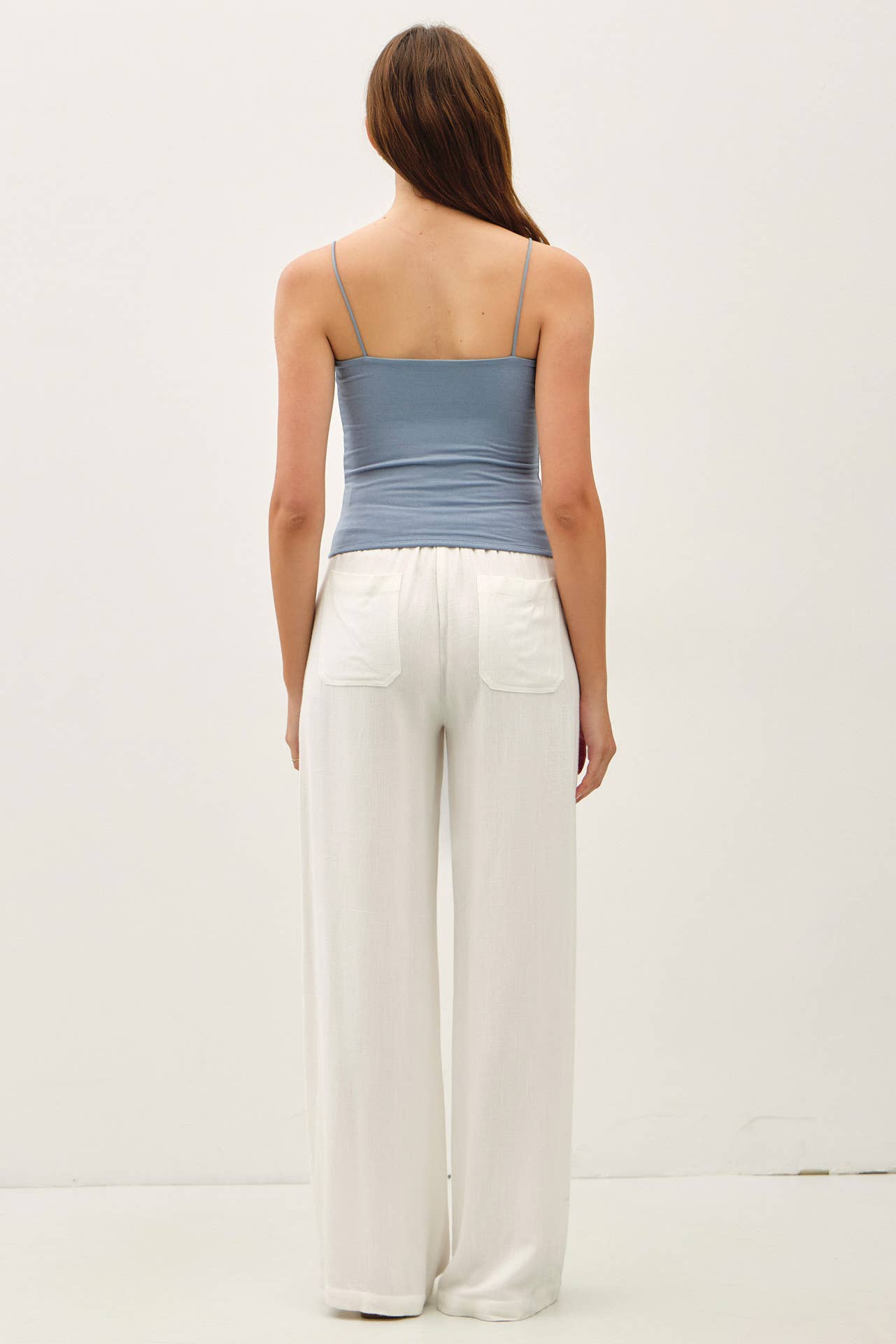 Woman wearing a blue tank top and white pants on a plain background