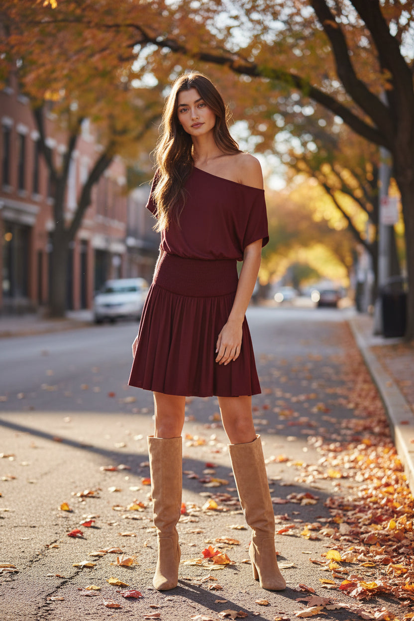 Woman wearing a burgundy one-shoulder dress against a textured wall.