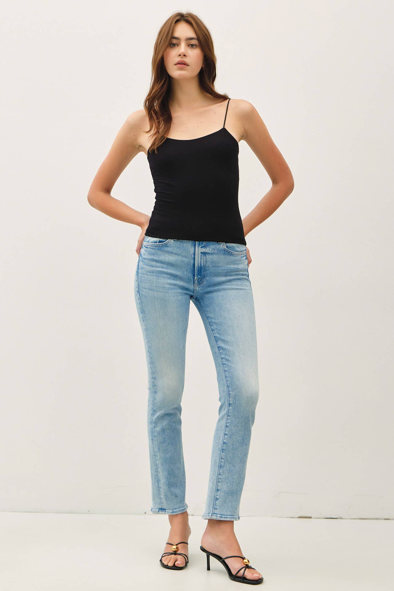 Woman wearing a black tank top and light blue jeans on a white background