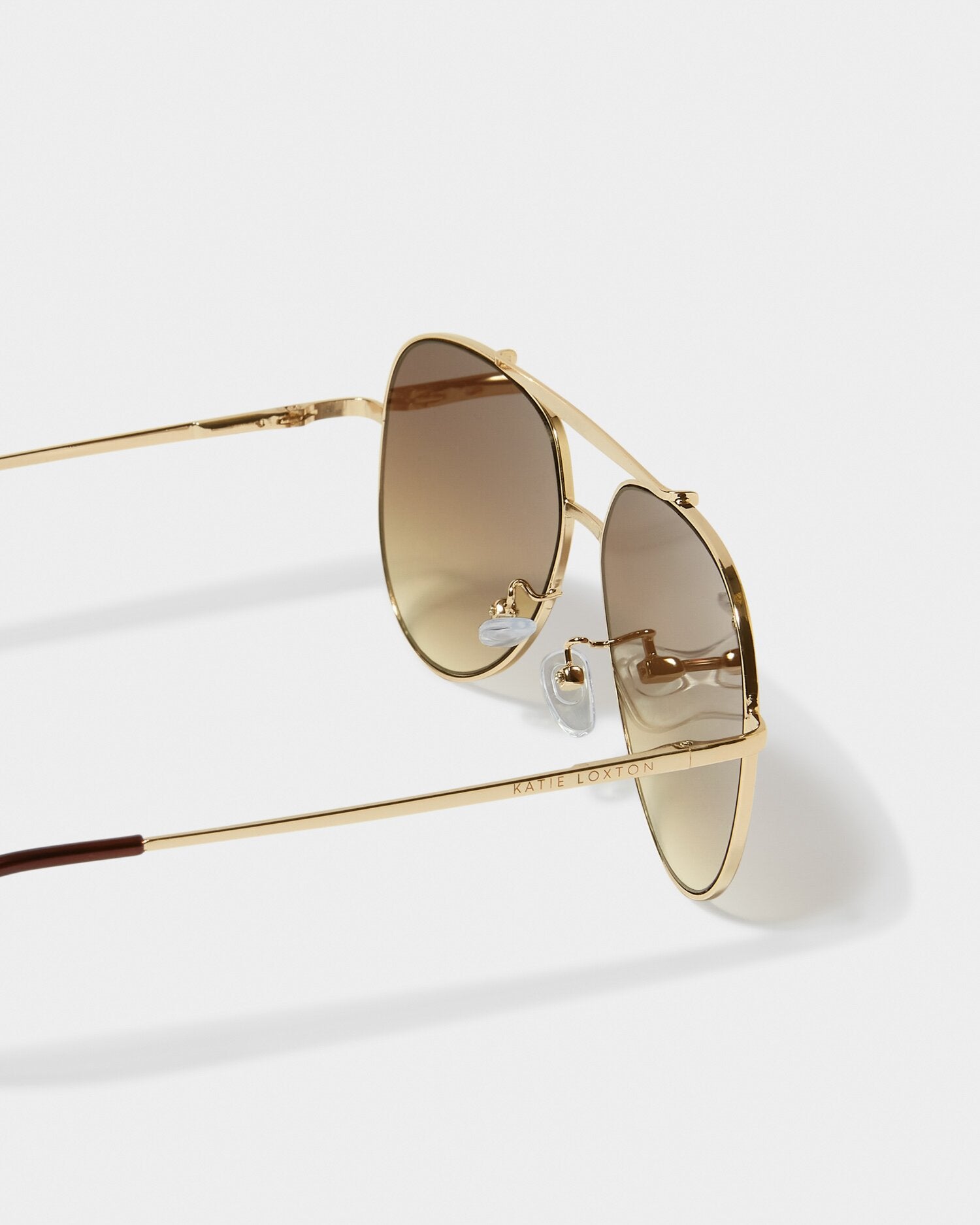 Gold-framed sunglasses with brown lenses on a light gray background