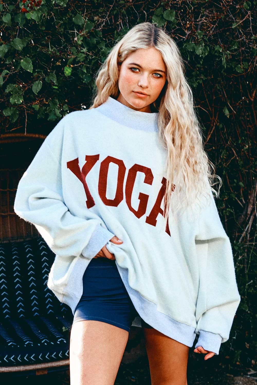 Woman wearing a light gray sweatshirt with 'YOGA' printed in red, standing outdoors.
