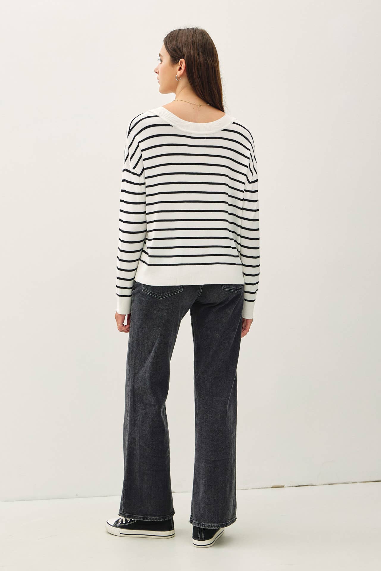 Person wearing a black and white striped sweater and dark jeans on a white background