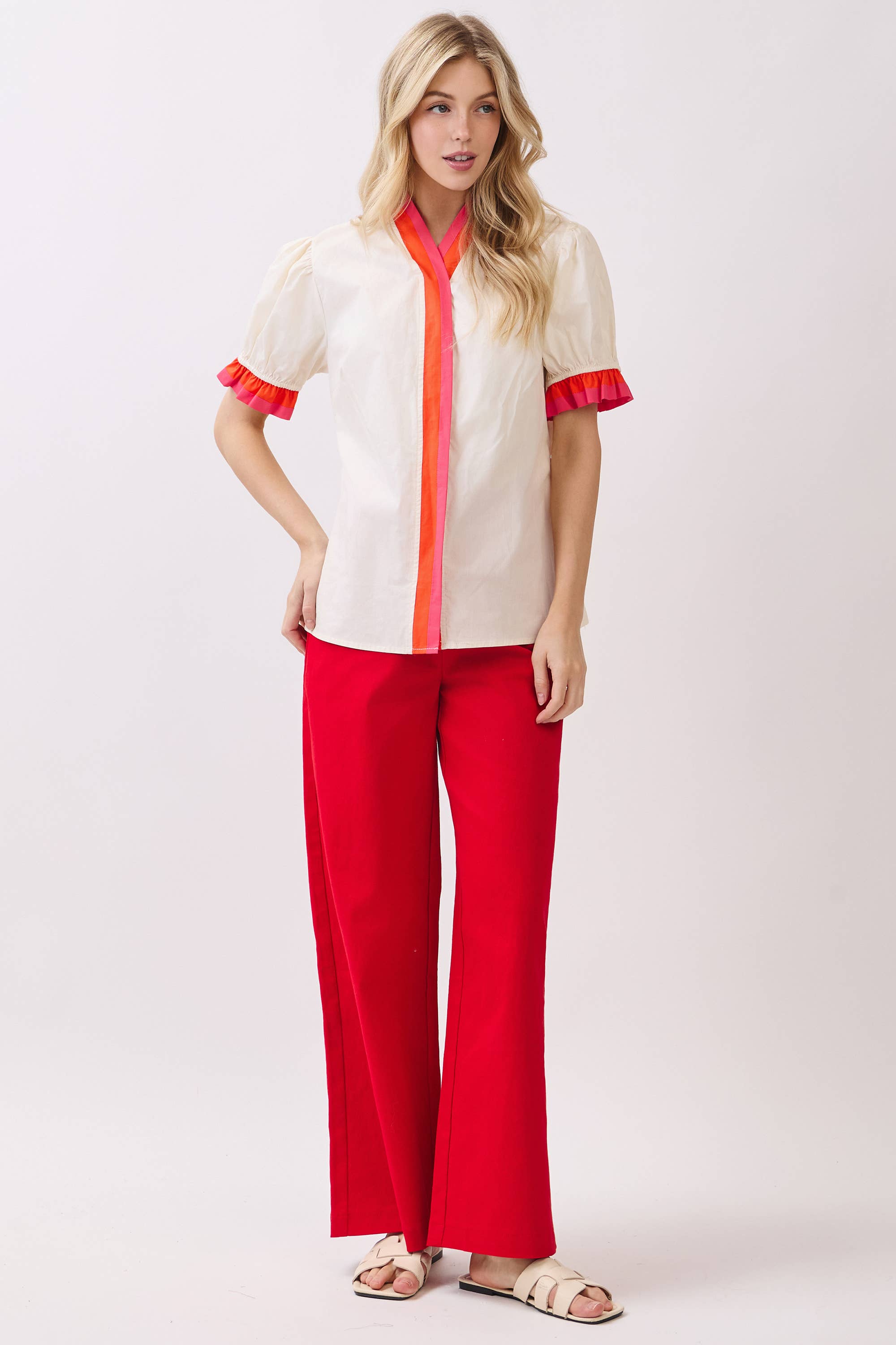 Woman wearing a white blouse with red accents and red pants on a white background