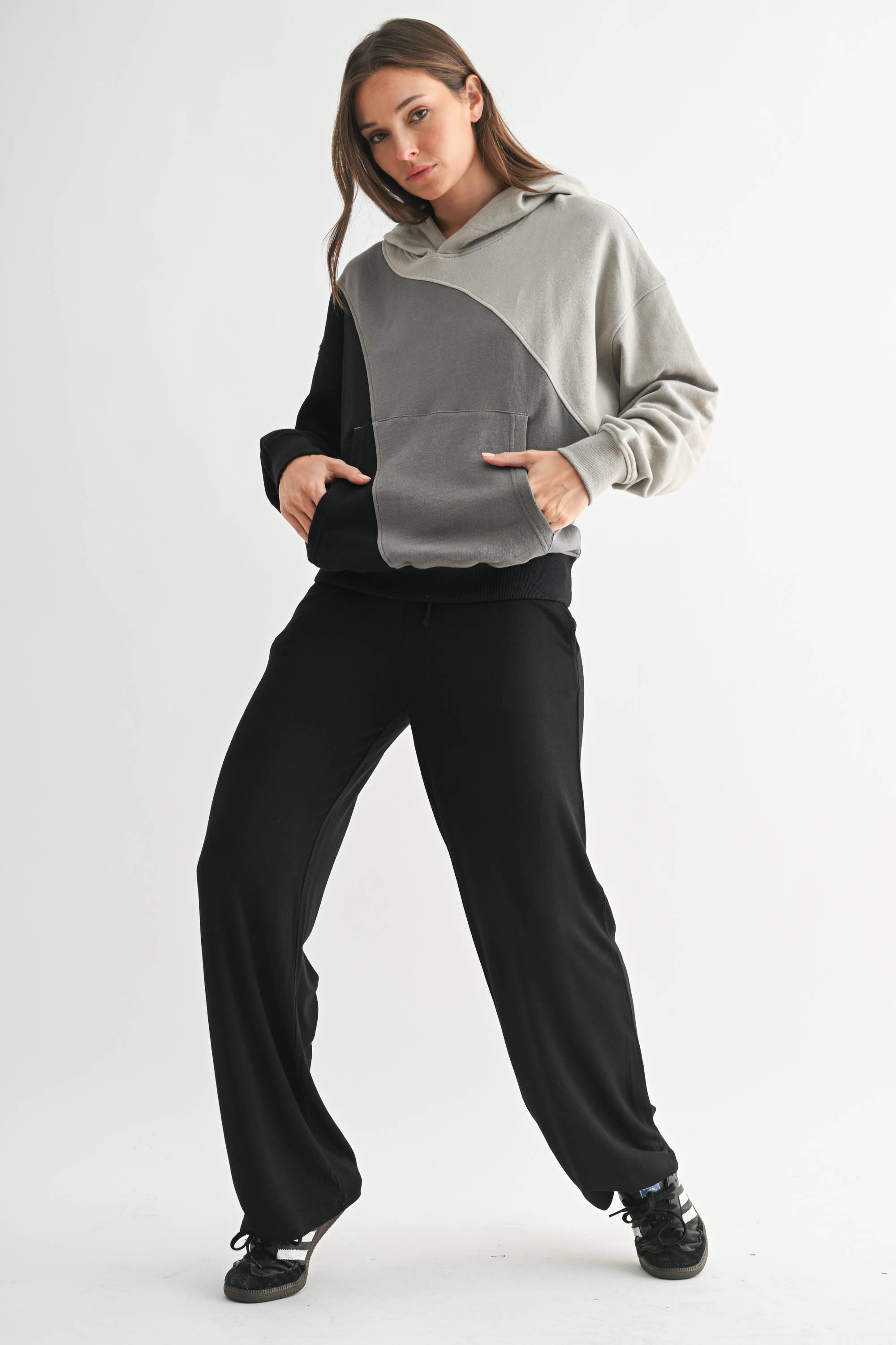 Woman wearing a gray and black color-blocked hoodie with black pants on a white background