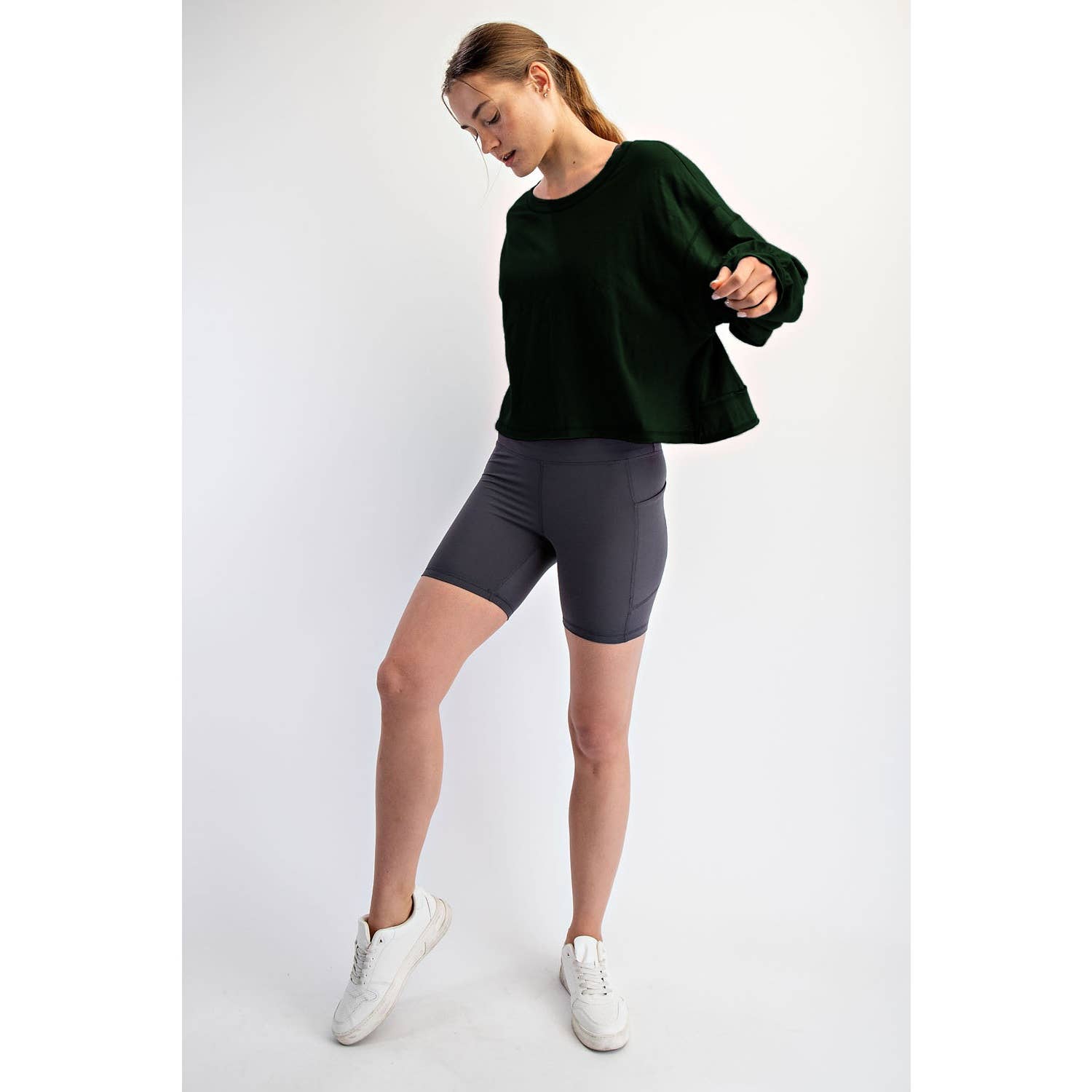 Woman wearing a dark green sweater and gray shorts on a white background