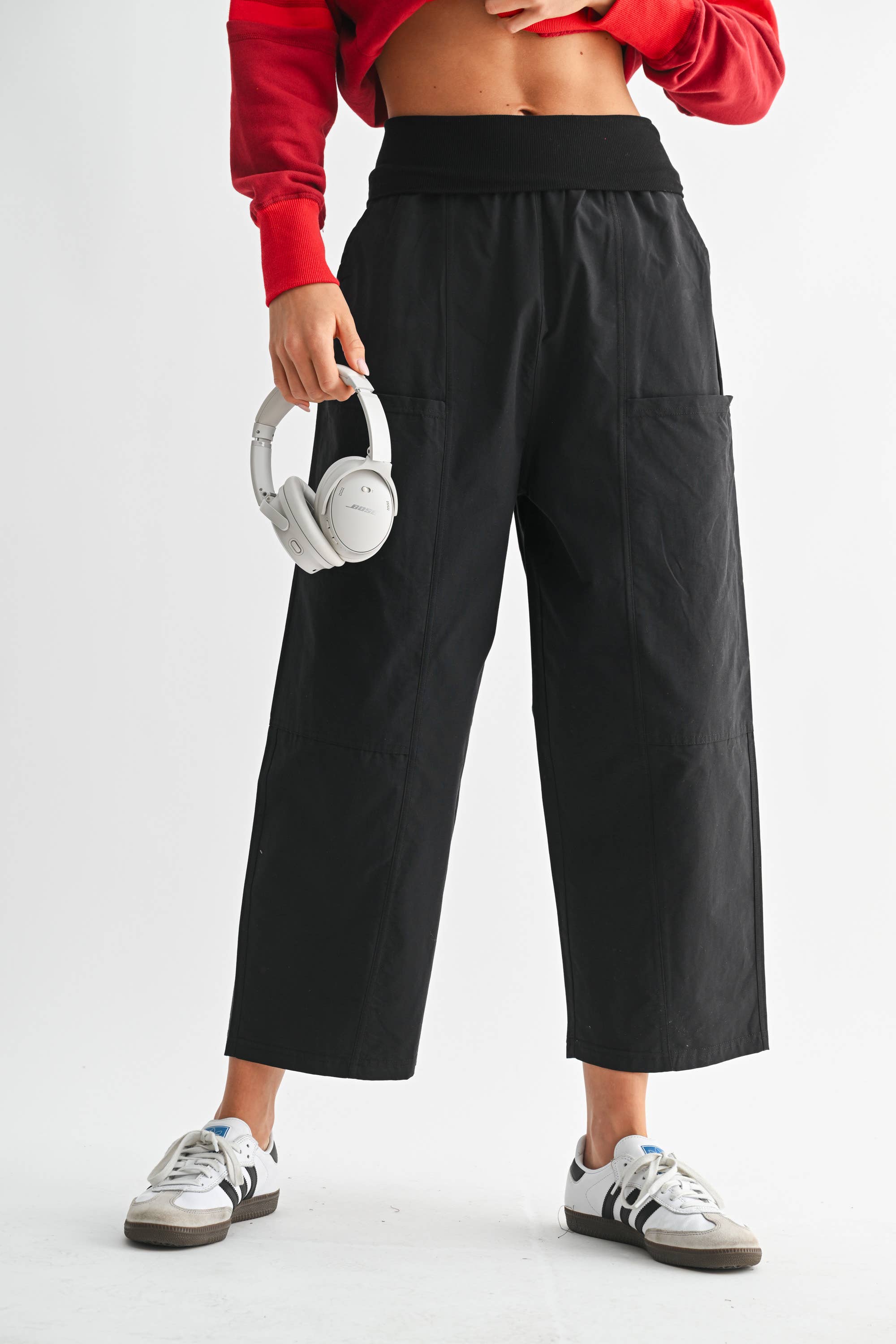 Person wearing black wide-leg pants and a red top, holding white headphones on a light gray background