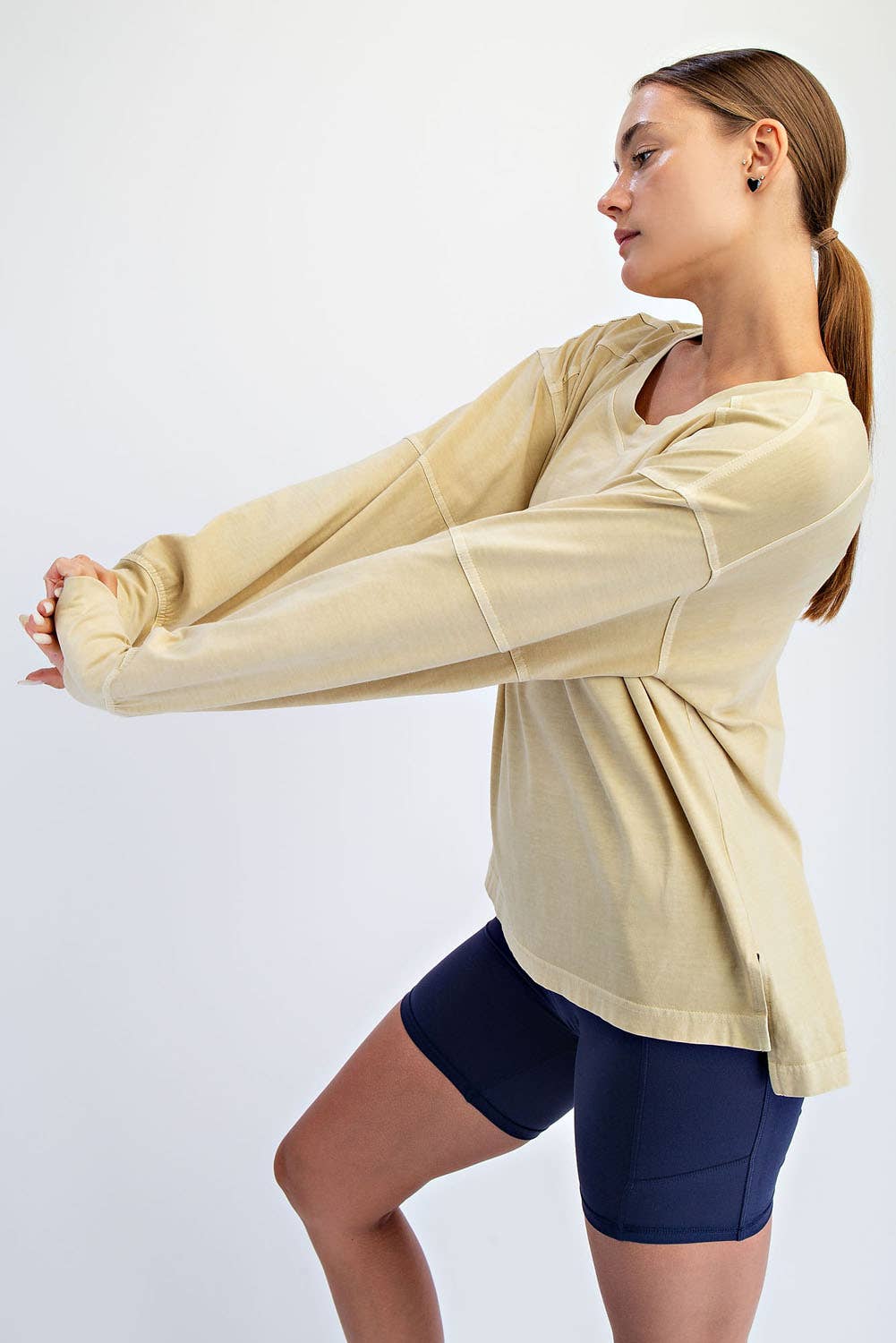 Woman wearing a beige long-sleeve shirt and navy shorts on a white background