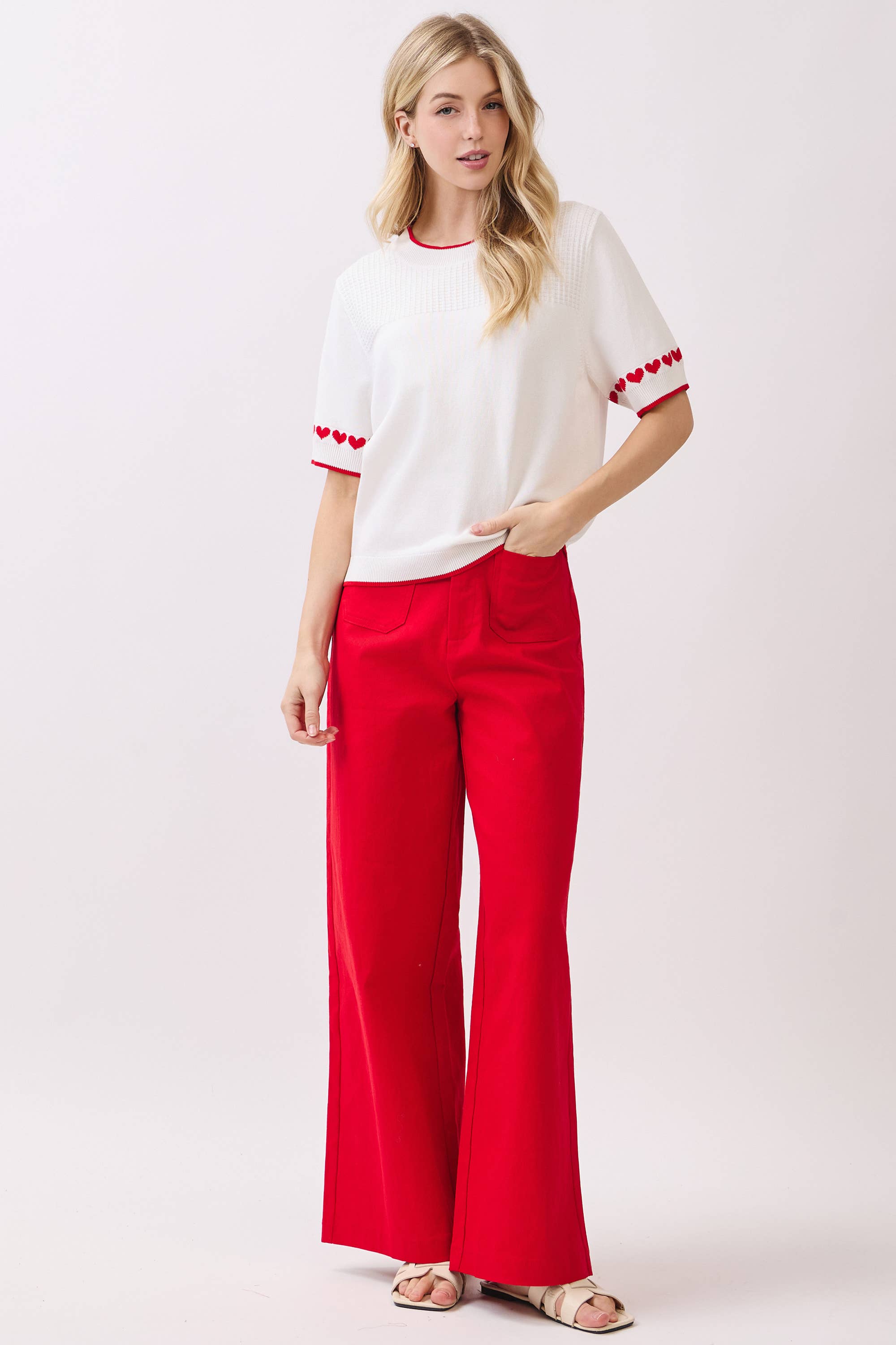 Woman wearing a white top with red accents and red pants on a white background