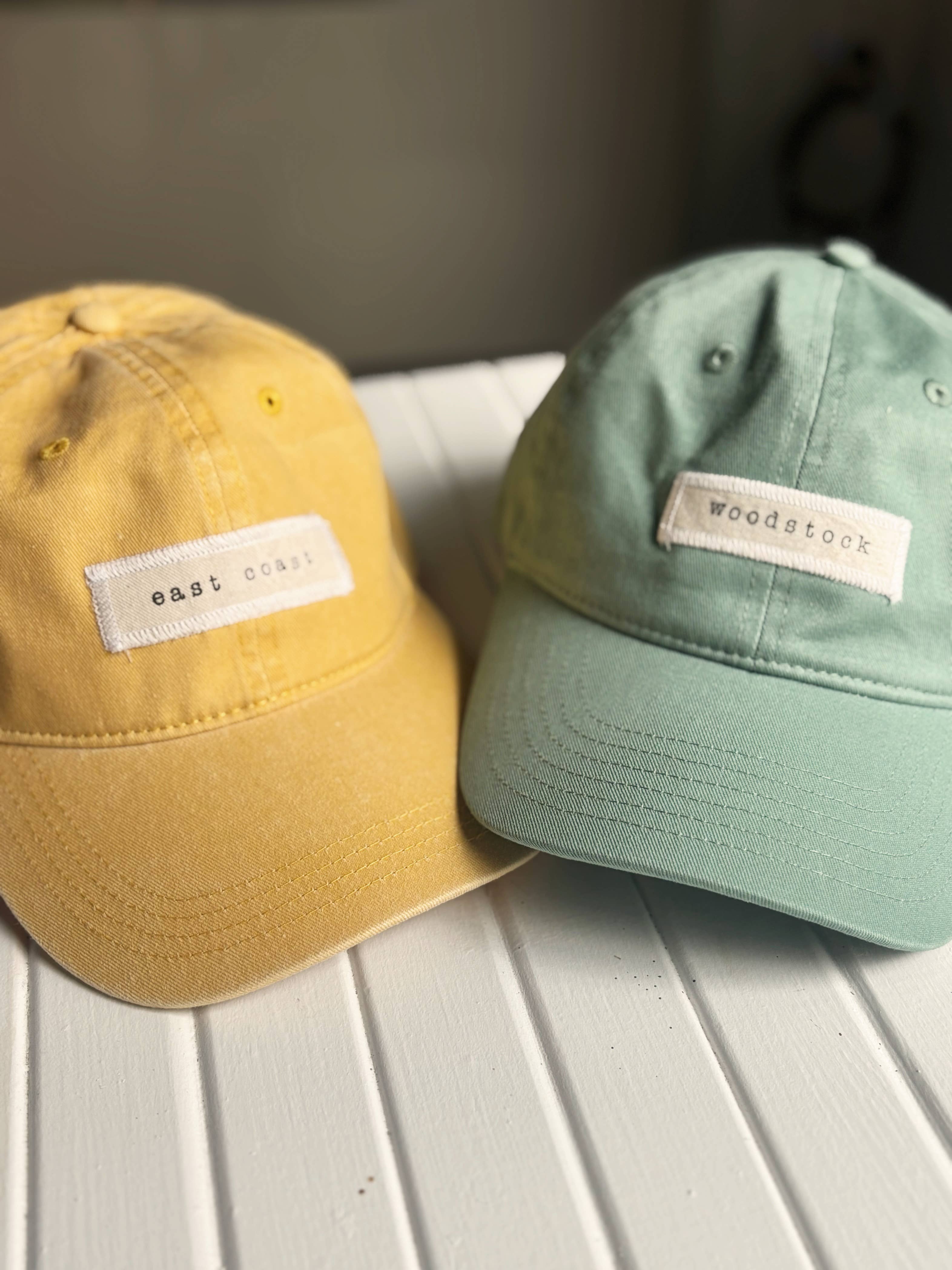Two baseball caps, one yellow and one green, with labels on a light wooden surface.