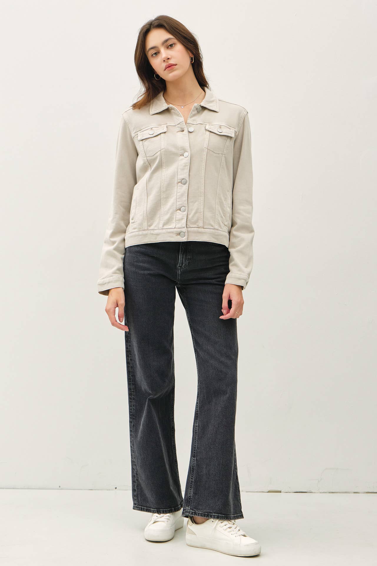 Person wearing a beige denim jacket and dark jeans on a white background