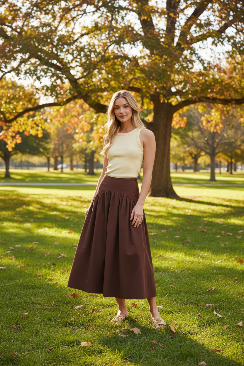 Woman wearing a yellow top and brown skirt in a park on a sunny fall day