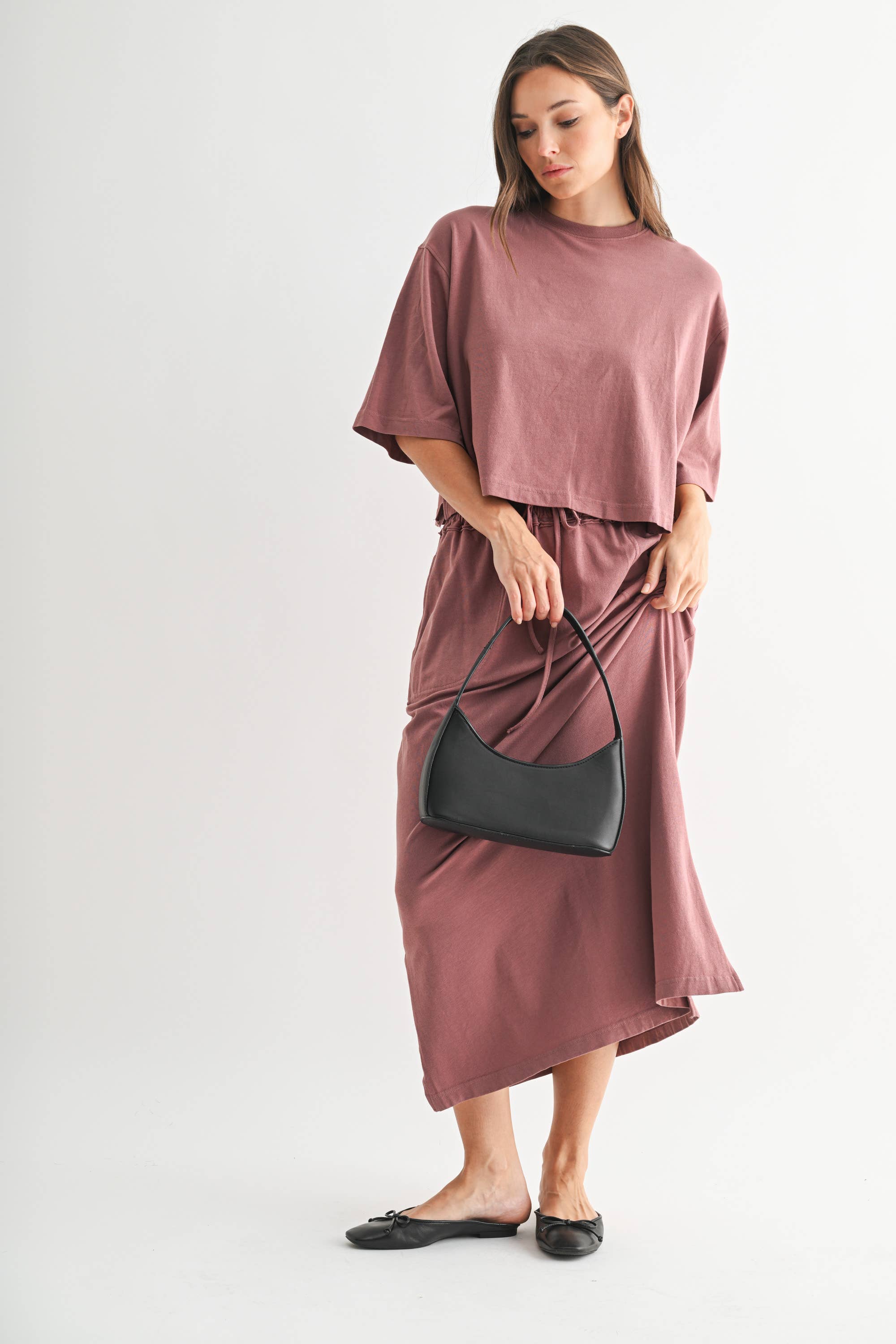 Woman wearing a mauve outfit with a black handbag on a white background