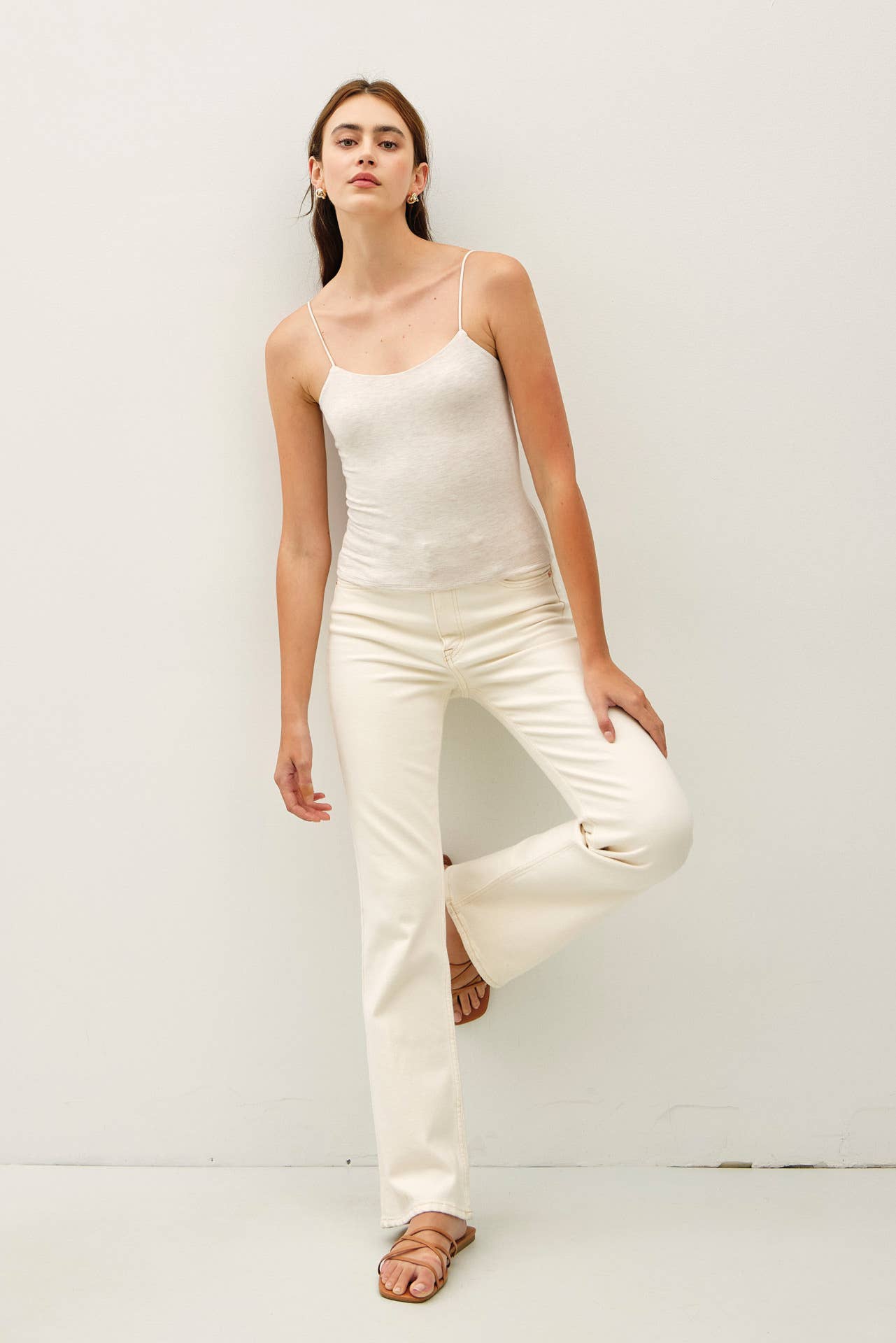 Woman wearing a white sleeveless top and pants against a white background