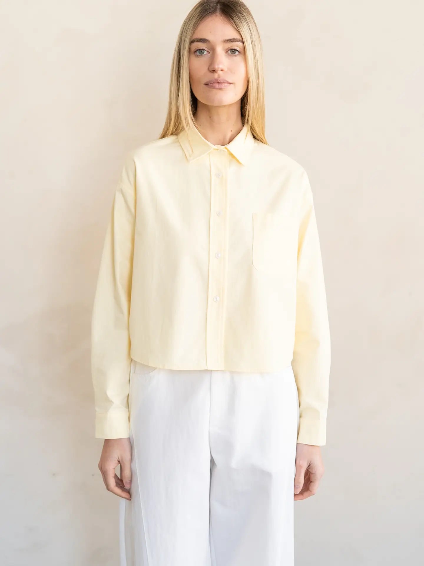 Woman wearing a light yellow blouse and white pants against a plain background