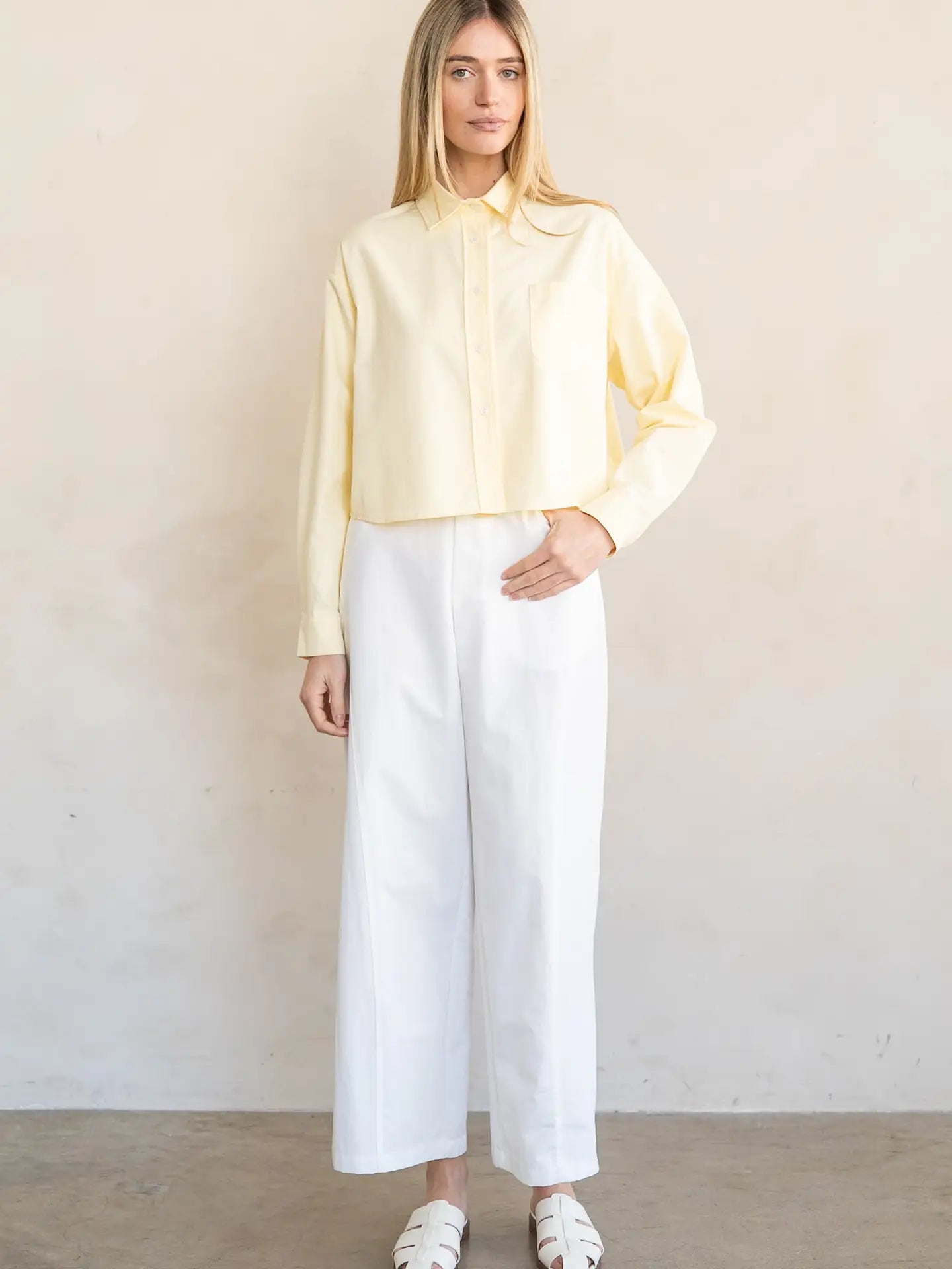 Woman wearing a light yellow blouse and white pants against a plain background