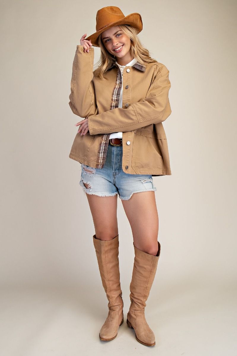 Woman wearing a tan jacket, plaid shirt, denim shorts, and tan knee-high boots on a beige background