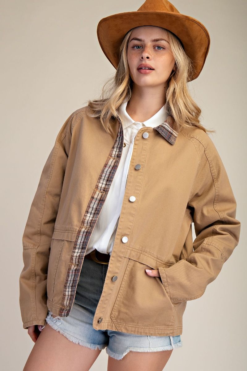 Woman wearing a tan jacket with plaid lining, white shirt, and denim shorts on a beige background