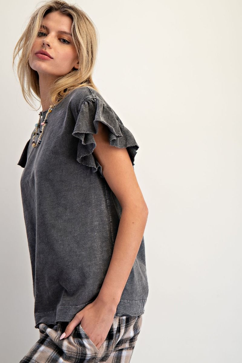 Woman wearing a dark gray ruffled sleeve top with plaid pants on a white background