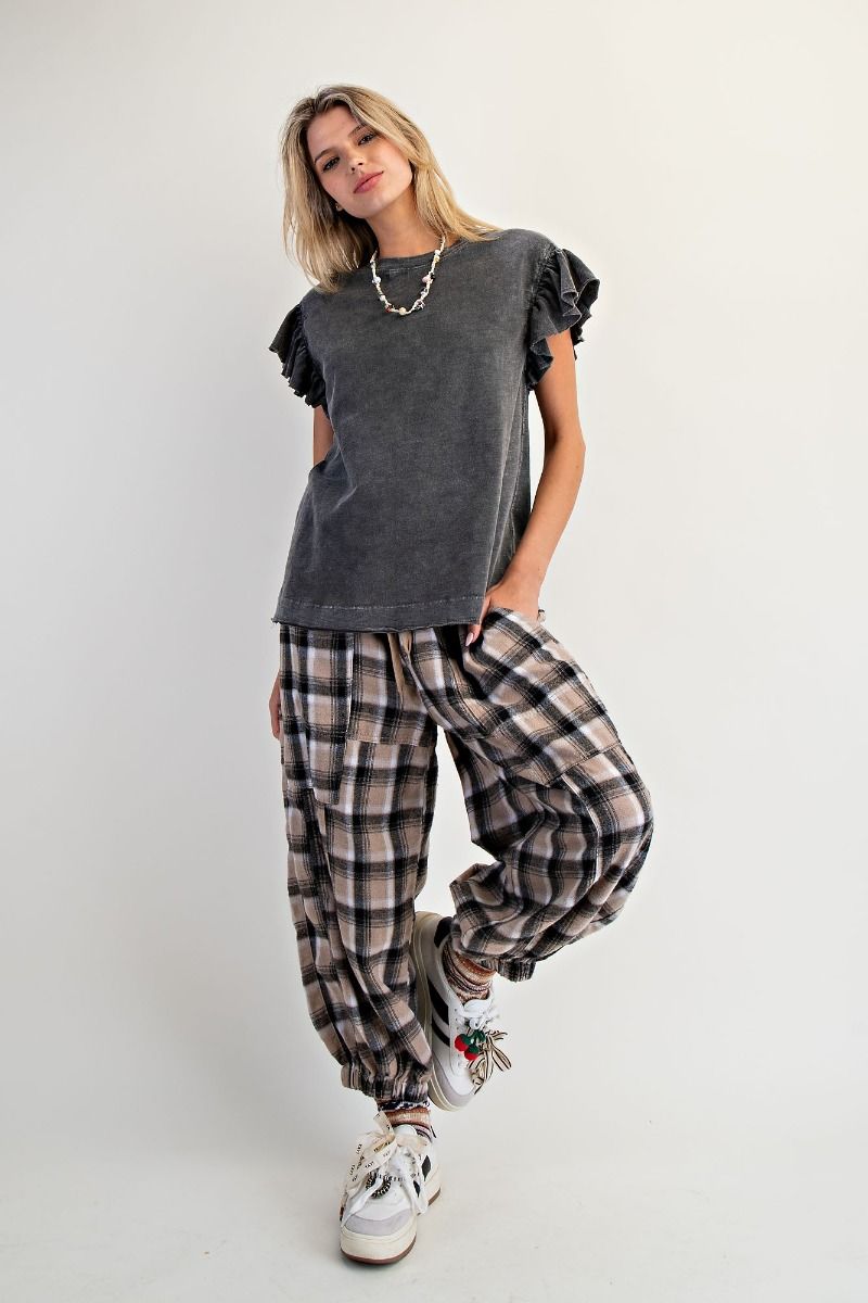 Woman wearing a gray ruffled top and plaid pants on a white background