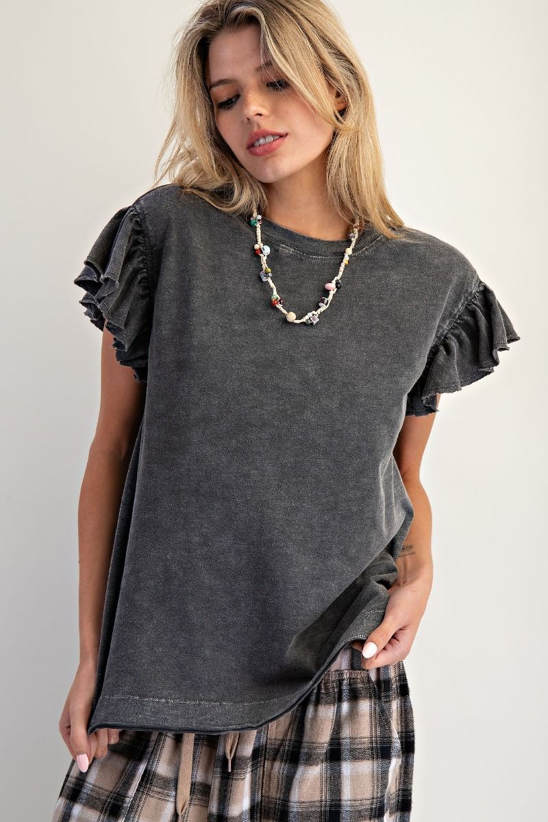 Woman wearing a dark gray ruffled sleeve top and plaid pants on a plain background