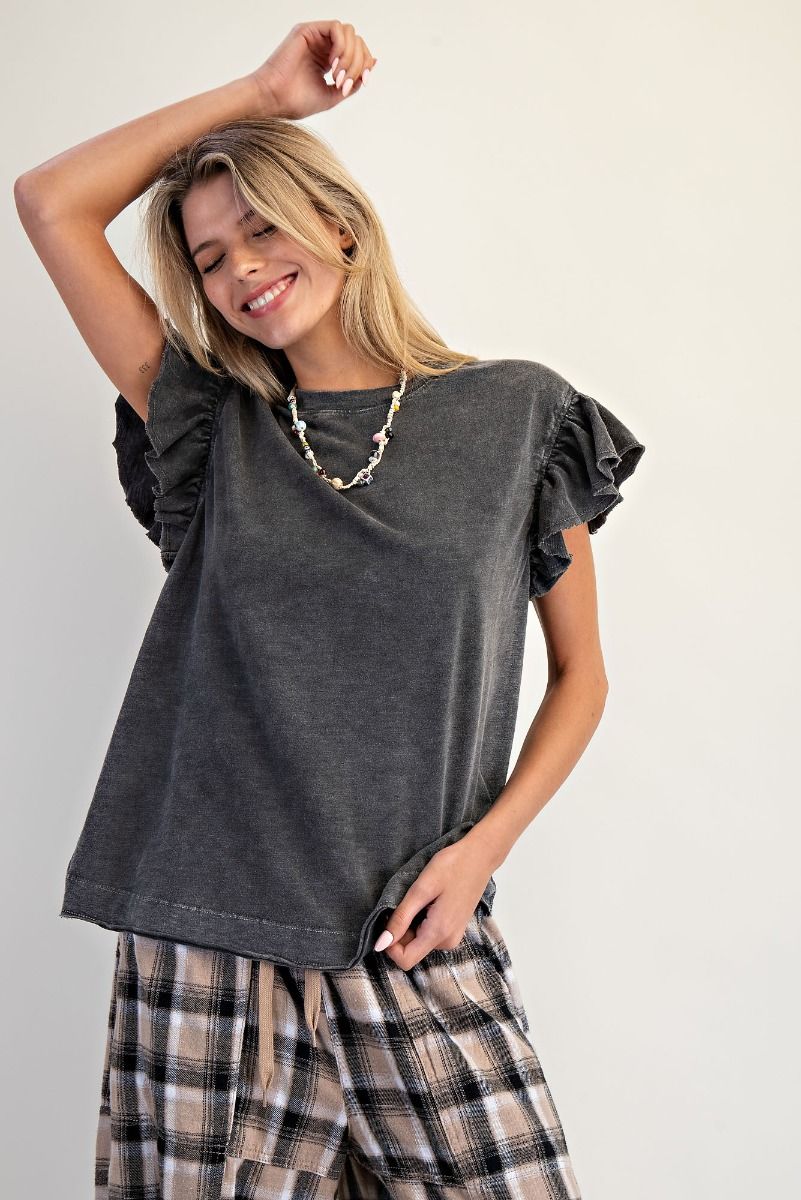 Woman wearing a Easel brand dark gray ruffled top and plaid pants on a white background