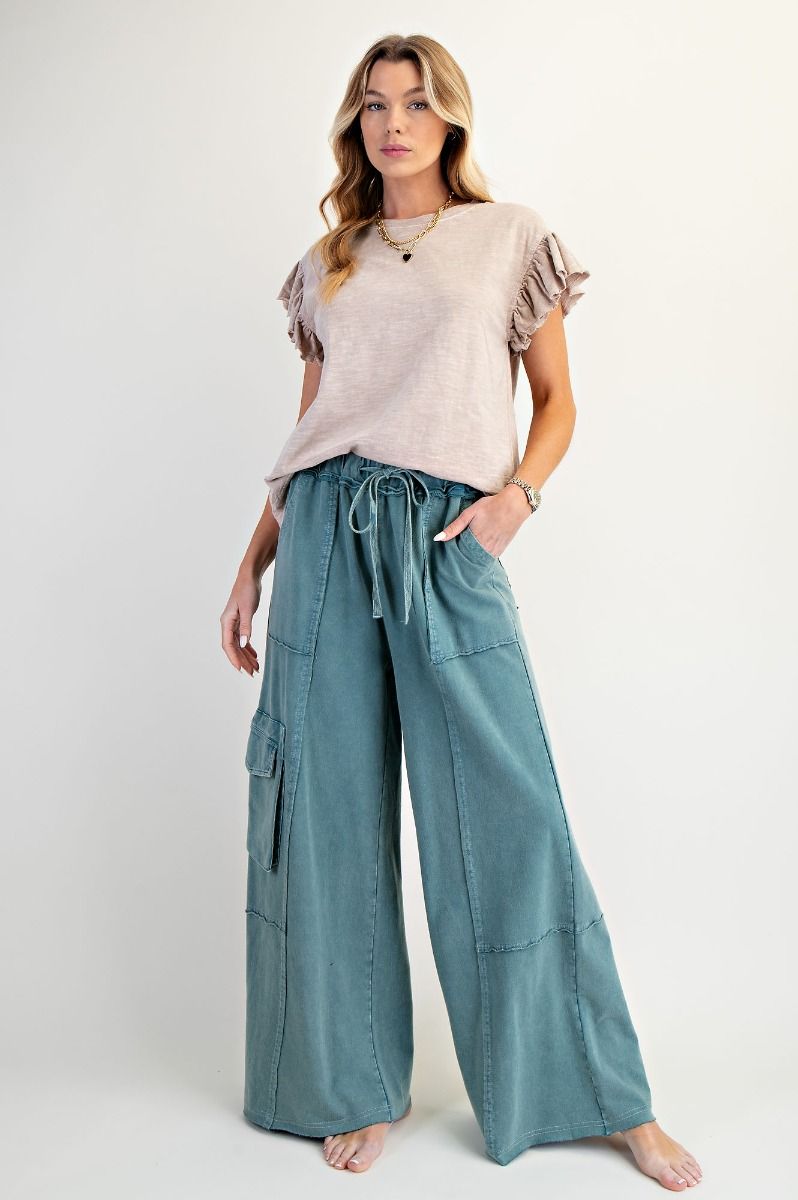Woman wearing a beige top and teal wide-leg pants on a white background